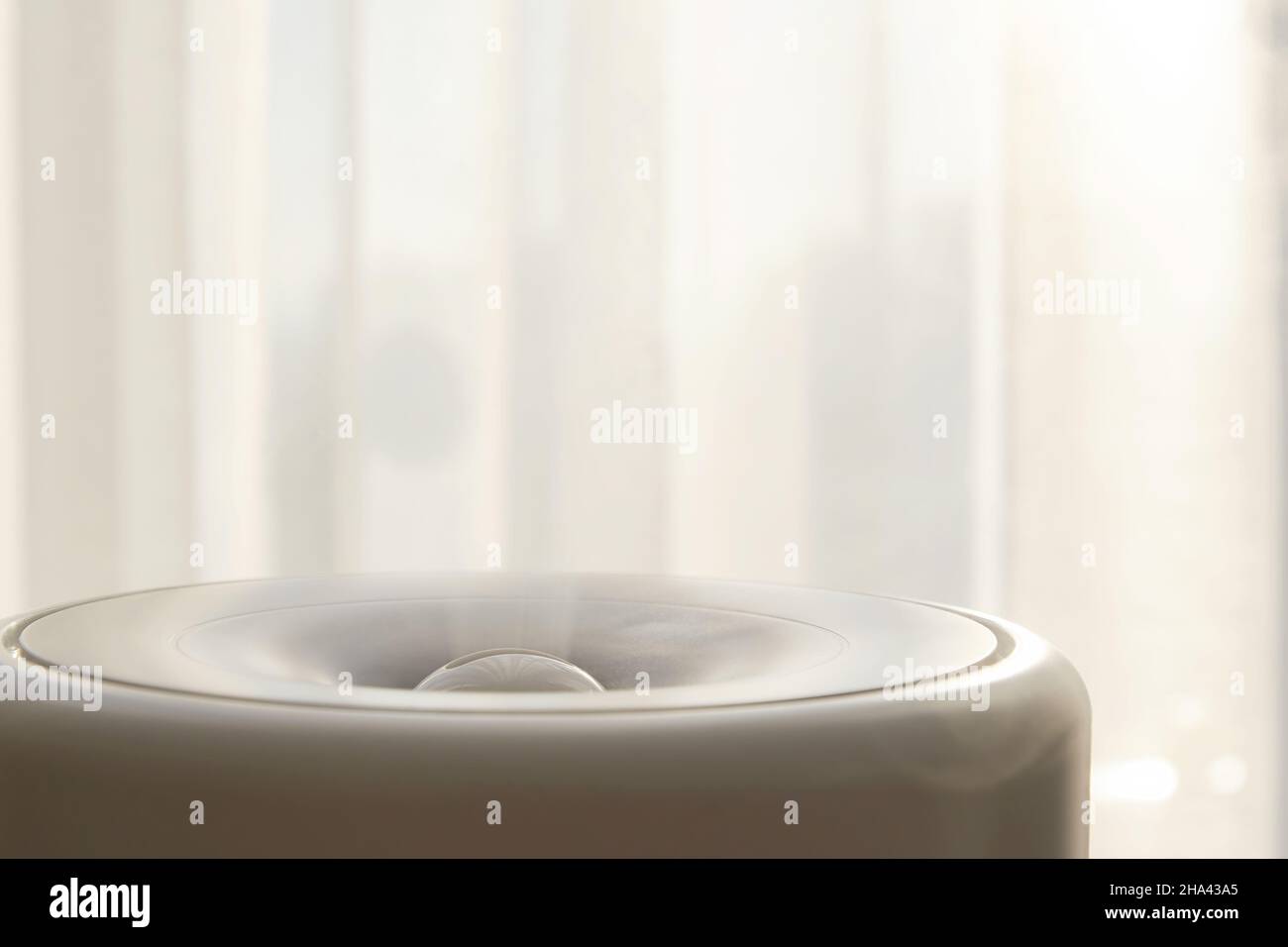 Elektrischer Luftbefeuchter mit Dampf gegenüber den Vorhängen im Schlafzimmer. Gemütlichkeit und Komfort zu Hause Stockfoto