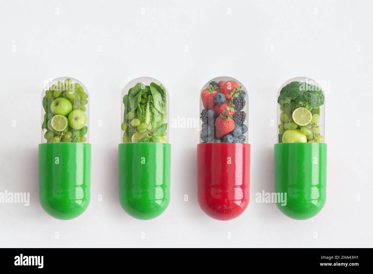 Rote Vitaminkapsel mit antioxidativen Beeren, die sich unter den grünen Pillen absticht Stockfoto
