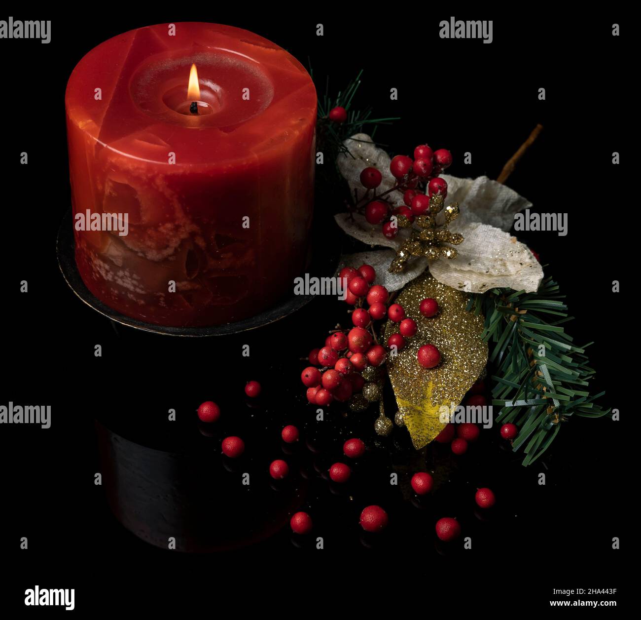 Schöne Weihnachtsdekoration mit brennender roter Kerze, roten Beeren und goldenem Blatt auf reflektierendem, glänzend schwarzem Hintergrund Stockfoto