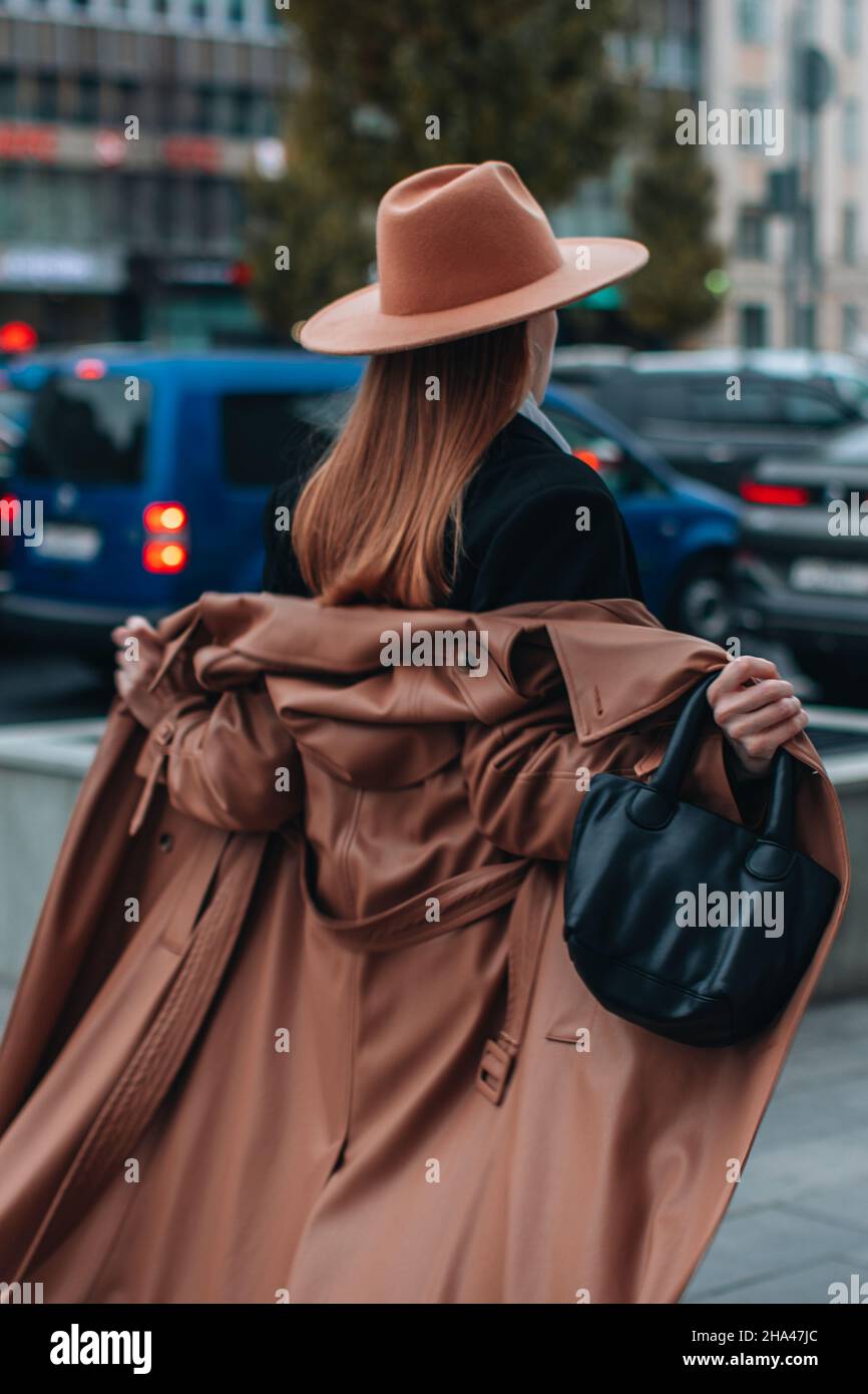 Frau in beigefarbenem Hut und langem braunen Ledermantel im Herbst, die in der Stadt spazieren geht. Damenmode im Street-Stil Stockfoto