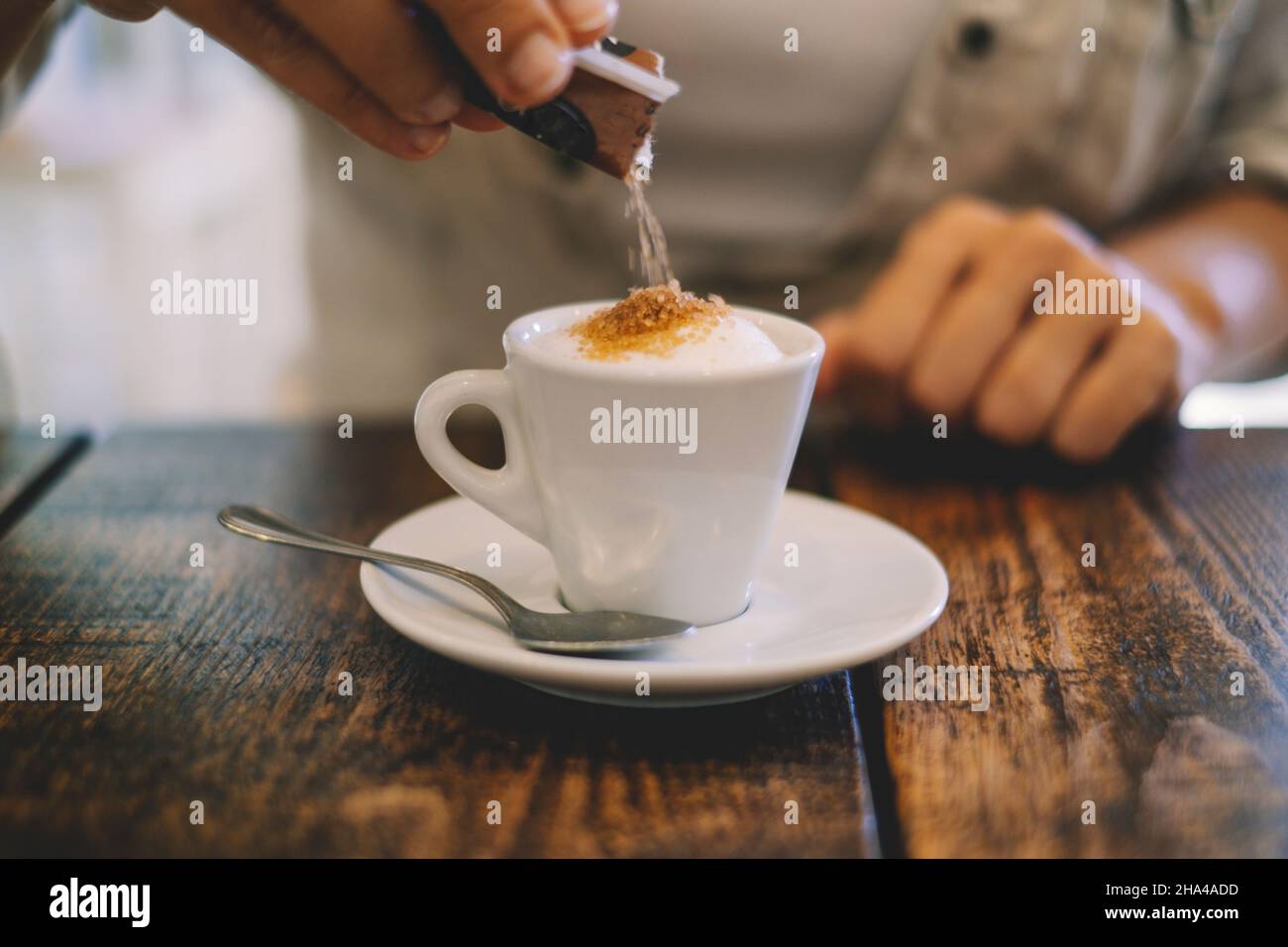 Nahaufnahme der Hände, die weißen Zucker in einen italienischen Espresso-Kaffee an der Bar oder im Restaurant auf einem Holztisch legen. italienische Tradition und arabisch. Freizeitbeschäftigung im Café und Frühstück am Morgen Stockfoto