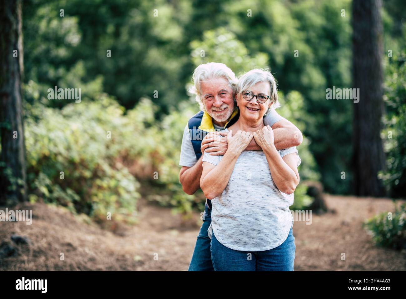 Romantisches liebendes glückliches Seniorenpaar, das sich umarmt, während es im Wald steht, lächelnder Mann, der Frau von hinten umarmt Porträt eines romantischen alternden alten Paares, das Freizeit im Wald verbringt Stockfoto