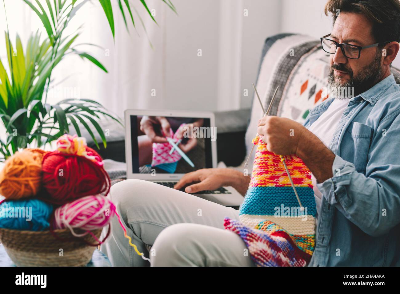 Moderner Mann in alternativen Freizeitaktivitäten in Innenräumen verwenden Laptop-Computer zu Online-Klasse der Strickarbeit mit Wolle zu sehen. Erwachsene Menschen und entspannen Hobby Zeit zu Hause. Traditionelle klassische Strickarbeit Stockfoto