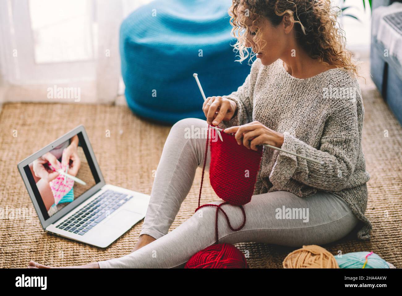 Eine Frau zu Hause auf dem Teppich sitzen Uhr online stricken Arbeit Tutorial und genießen Wollstricken Aktivität Hobby. Menschen und Online-Content-Klasse Konzept Lifestyle. Kreative weibliche Leben Stockfoto