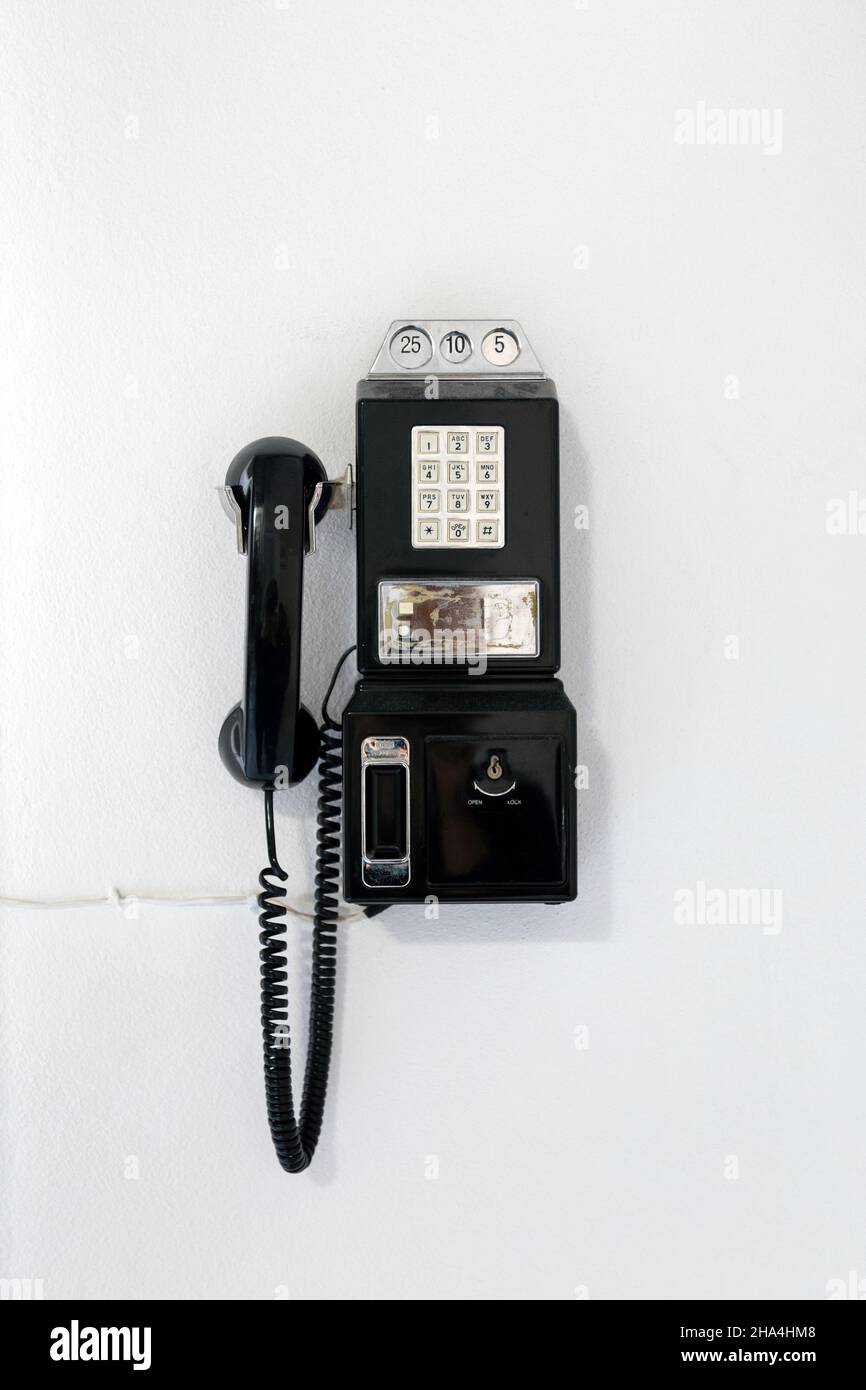 Schwarzes vintage Druckknopf-Payphone, das an der Wand hängt Stockfoto
