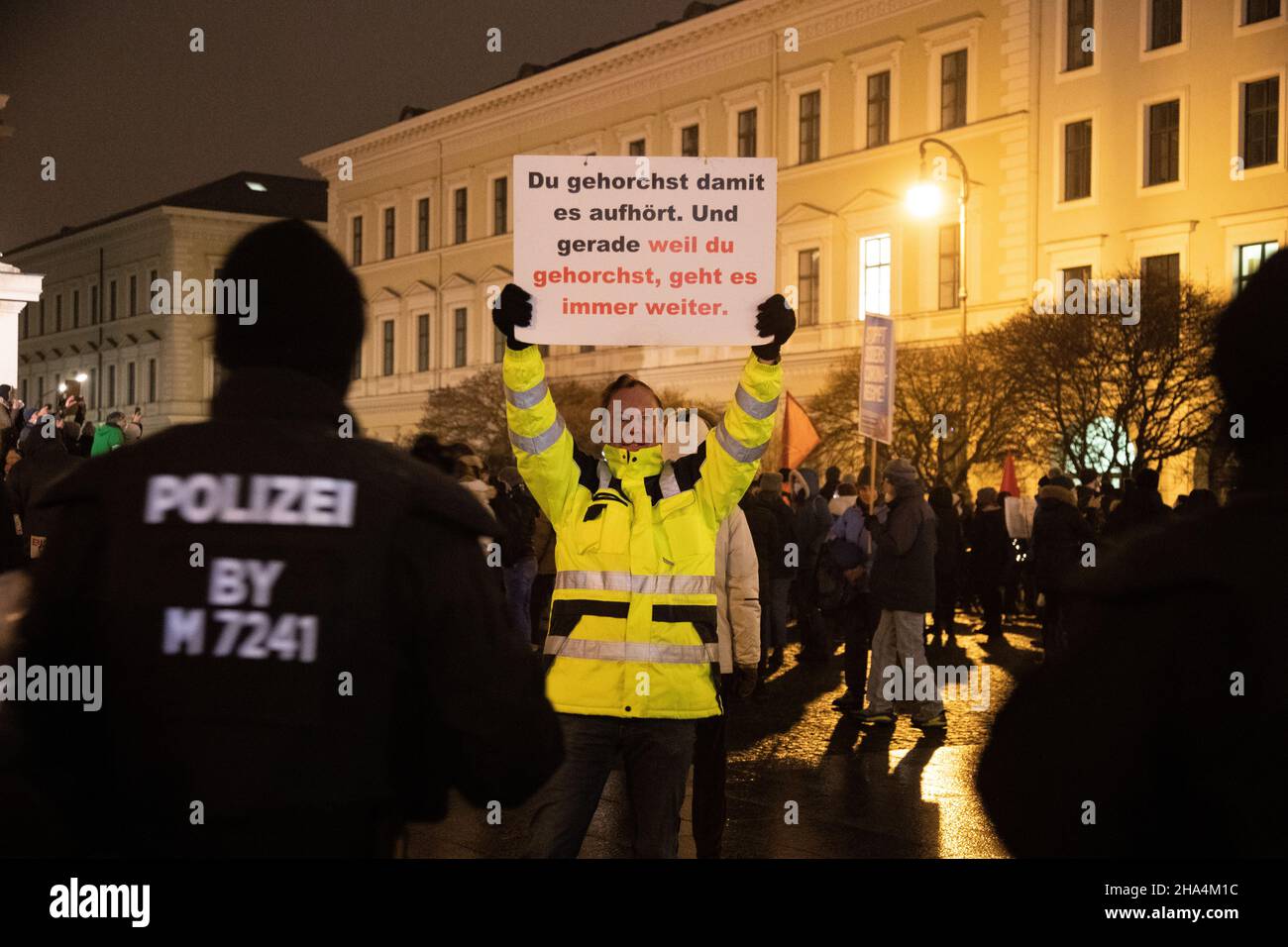 Protestor in gelber Jacke hält ein Schild hoch und trägt demonstrativ keine  Maske vor Polizisten. Am 8. Dezember versammelten sich 2021 1600-1800  Querdenker, Anti-Vaxx-Aktivisten und Verschwörungsideologen in München, um  gegen alle kovidierten