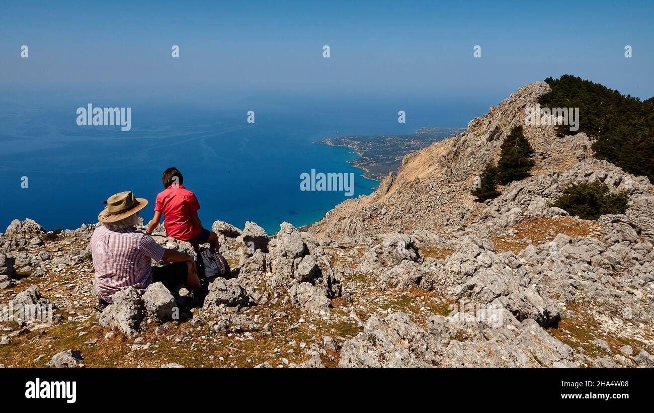 griechenland, griechische Inseln, ionische Inseln, kefalonia, Berg, enos, Gipfel, zwei Wanderer sitzen nicht weit vom Gipfel auf Felsen und blicken nach unten, Felsen, blaues Meer, blauer Himmel Stockfoto