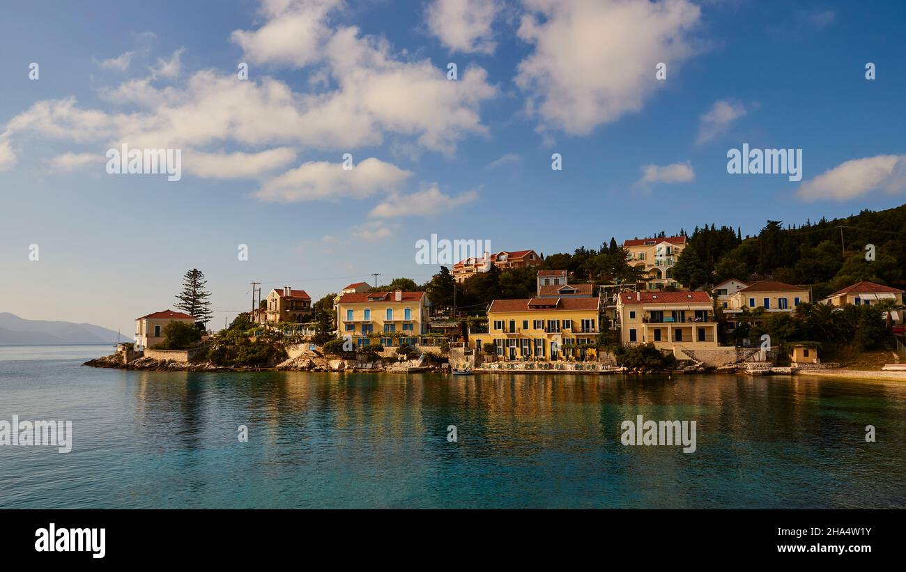 griechenland,griechische Inseln,ionische Inseln,kefalonia,fiskardo,Morgenstimmung,teils bewölktes Himmel,Morgenlicht auf fiskardo,südlicher Bezirk,Hafenbecken im Vordergrund dunkelgrün,himmeltiefblau mit isolierten weißen Wolken Stockfoto