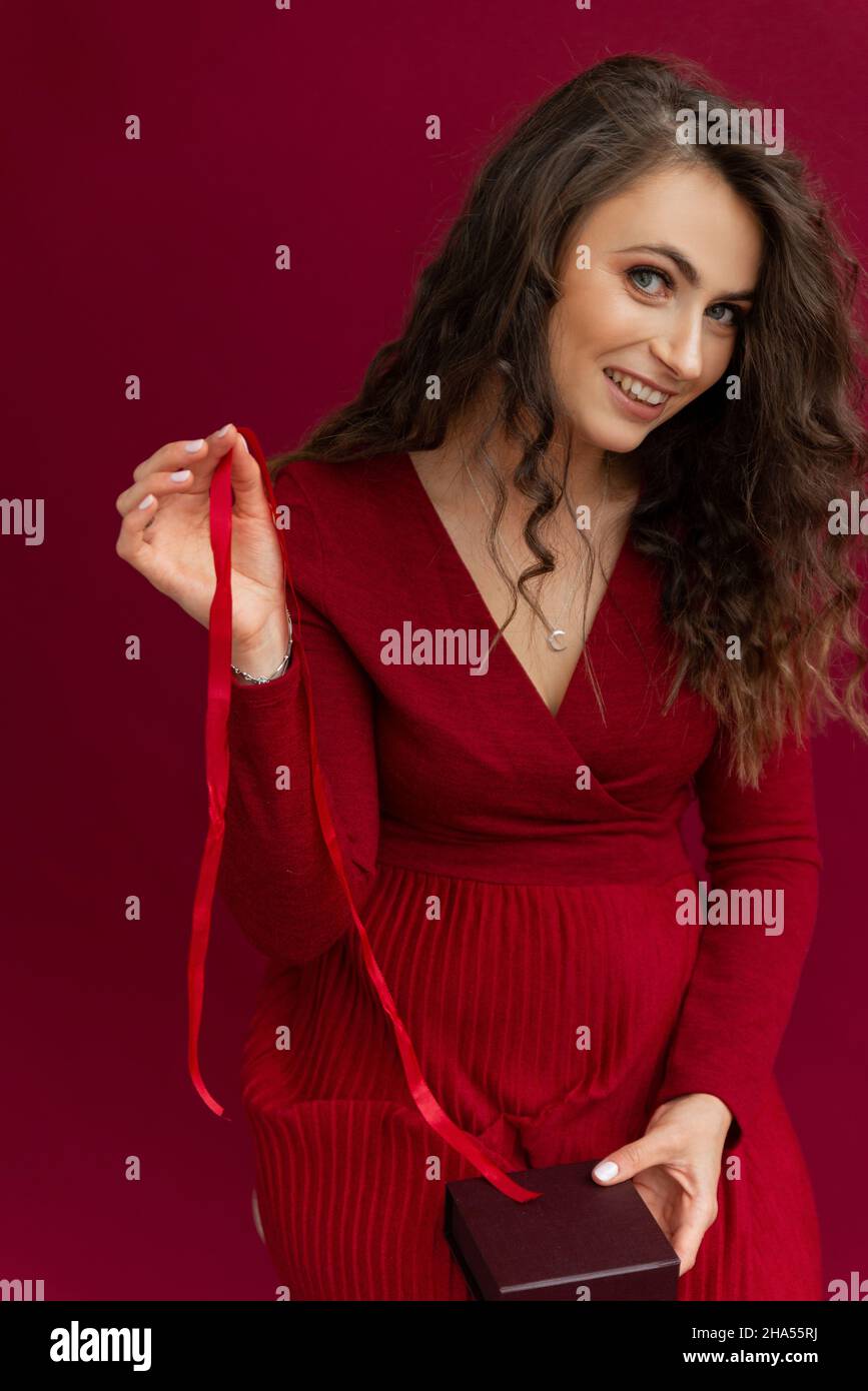 Lockige Frau in rotem Kleid geöffnet Box mit Streifen. Stockfoto