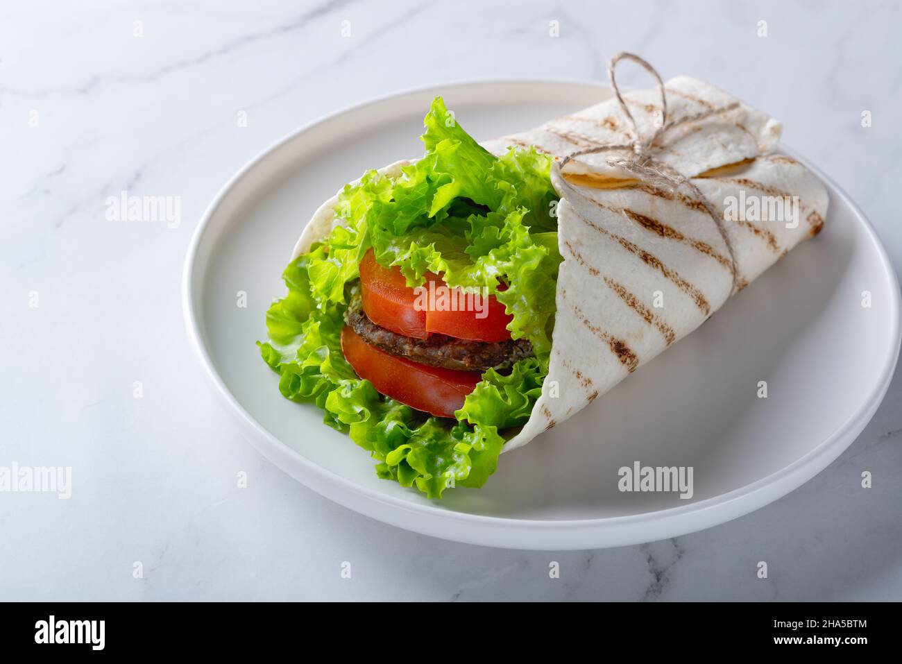 Sandwich mit Fleischsteak, Tomaten und Grünpflanzen auf Weiß einwickeln Stockfoto