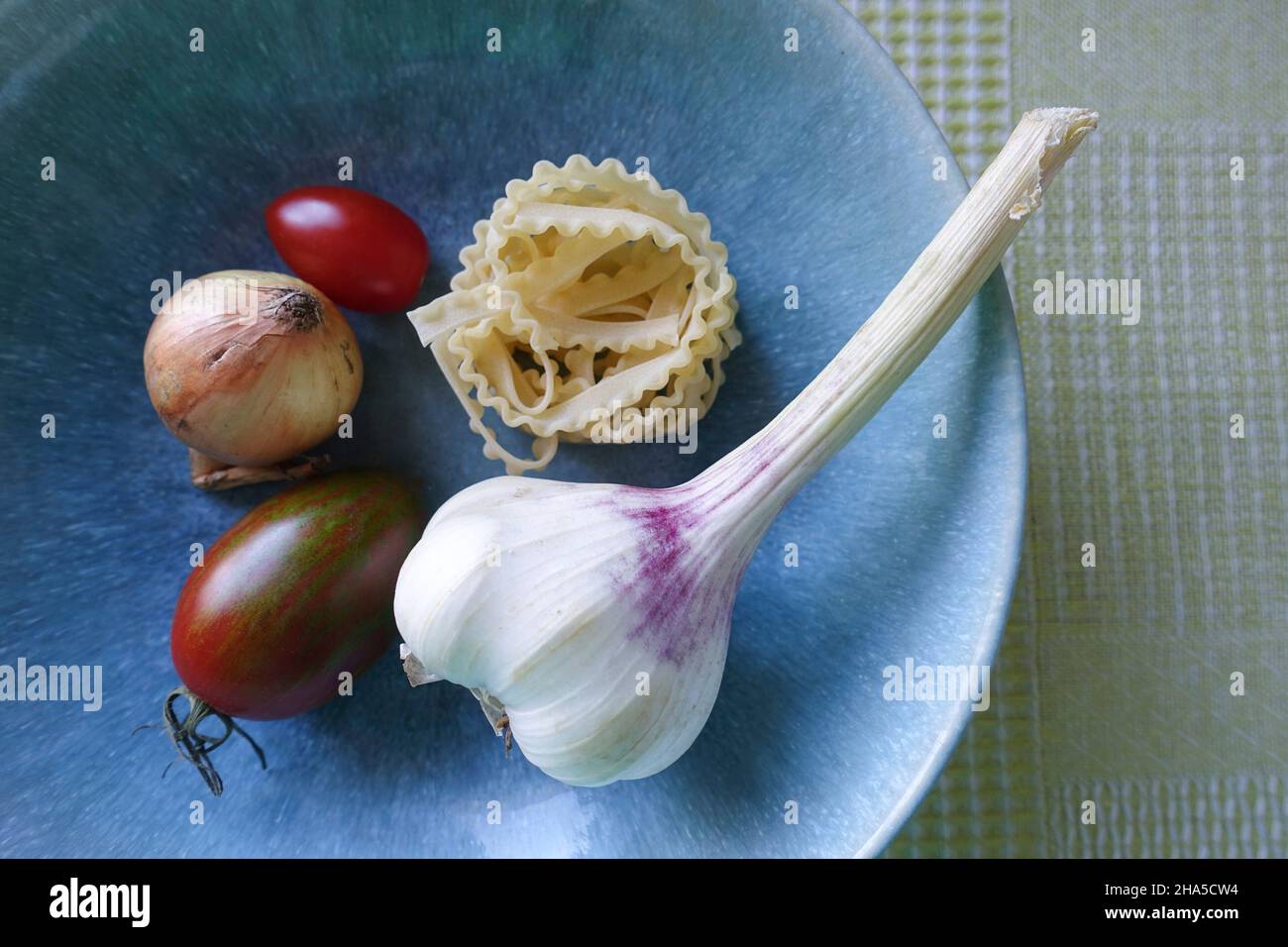 Blaue Schüssel mit Gemüse. Knoblauch, Tomaten, Nudeln und Zwiebeln, Zutaten für eine Pasta-Gericht. Stockfoto