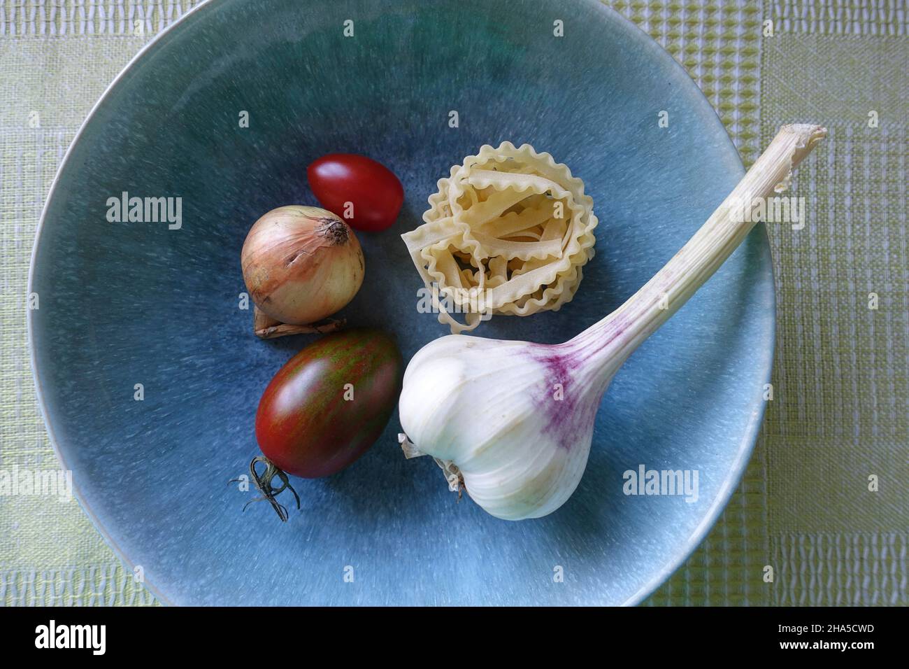 Knoblauch, Gemüse und Nudeln sind in einem blauen Teller. Zutaten für eine köstliche Pasta-Gericht. Stockfoto