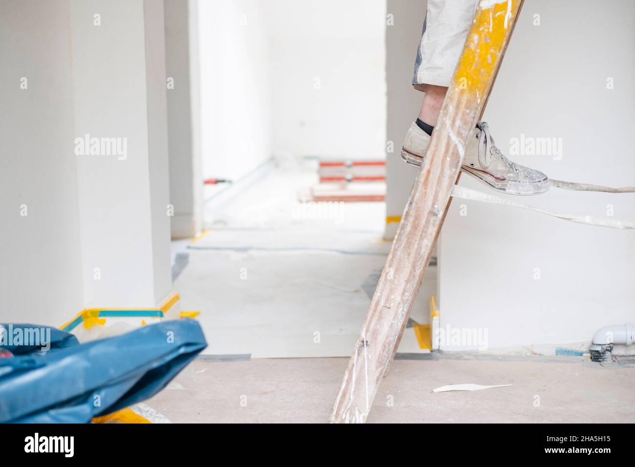 Baustelle, Sanierung und Renovierung einer Wohnung, Maler steht auf einer Leiter in einem leeren Raum Stockfoto