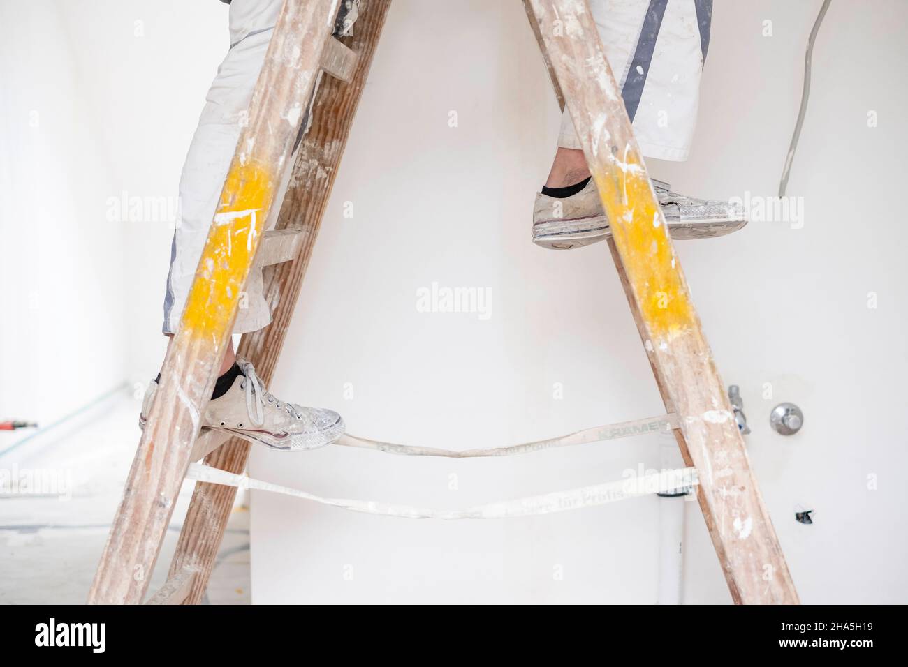 Baustelle, Sanierung und Renovierung einer Wohnung, Maler steht auf einer Leiter in einem leeren Raum Stockfoto