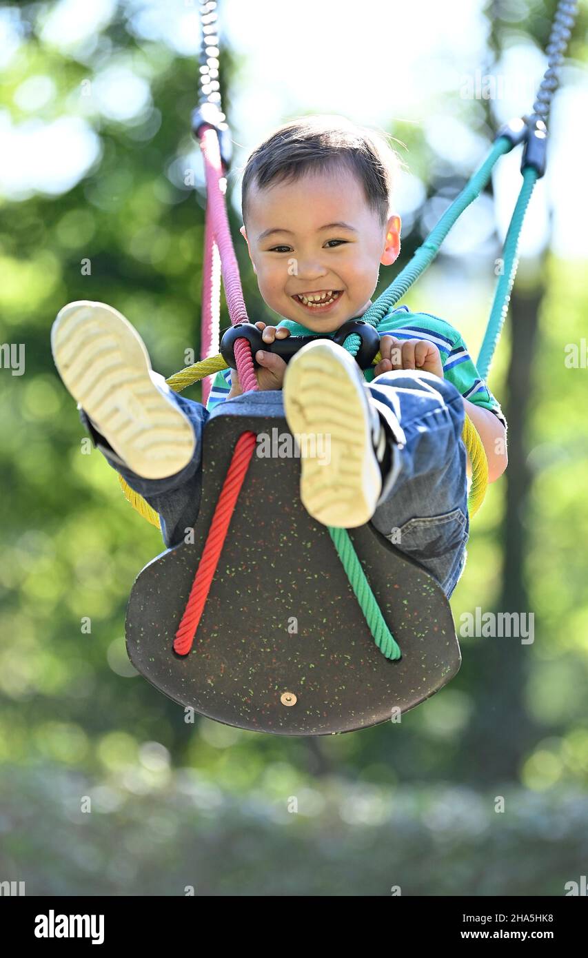 Kleinkind, 2 Jahre, multiethnisch, eurasisch, lacht, schaukelt auf einer Kinderschaukel, blaubeuren, baden-württemberg, deutschland Stockfoto