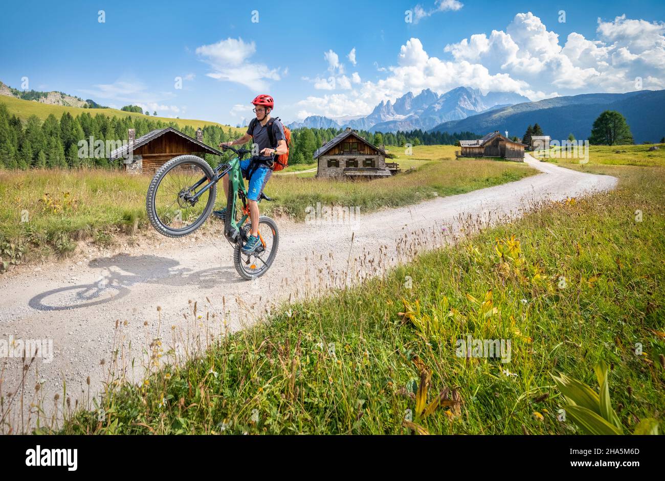 Radler auf dem E-Bike zwischen den fuciade Hütten mit dem Pale di san martino Gebirge im Hintergrund, Gemeinde soraga, trient, trentino, italien Stockfoto