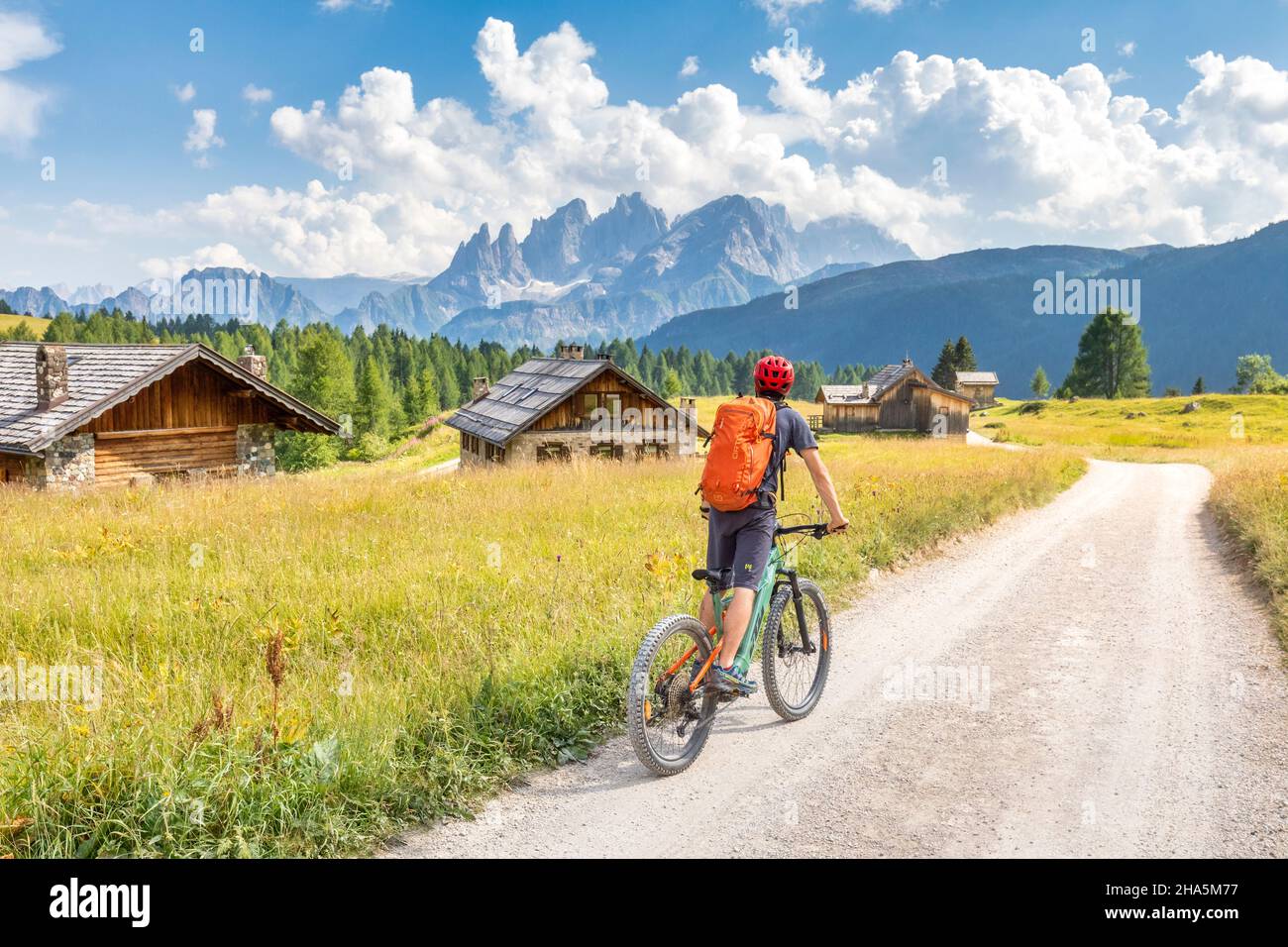 Radler auf dem E-Bike zwischen den fuciade Hütten mit dem Pale di san martino Gebirge im Hintergrund, Gemeinde soraga, trient, trentino, italien Stockfoto