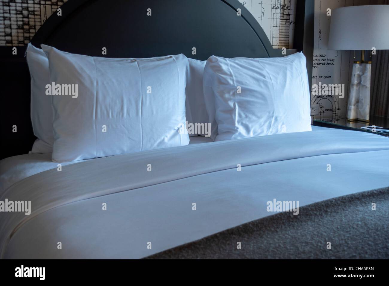 Schräg Blick auf ein sauber gemachtes Hotelbett, mit frischer weißer und grauer Bettwäsche und einem schwarzen Kopfteil Stockfoto