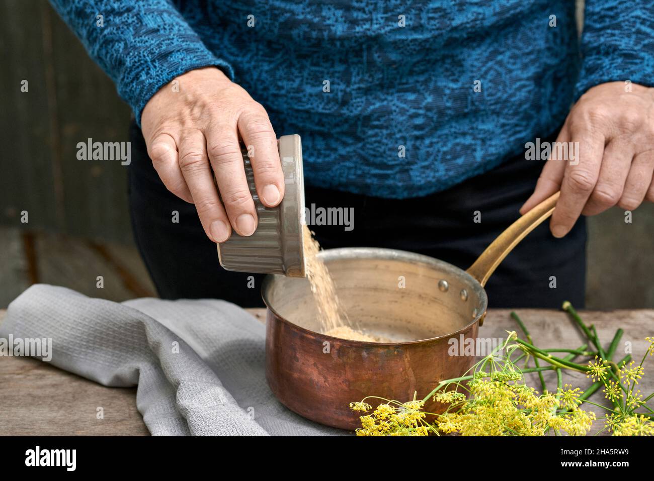 Arbeitsschritte mit Fenchel und Fenchelsamen für die Herstellung von Fenchelsaft füllt die Frau Rohrzucker in einen Kupfertopan Stockfoto