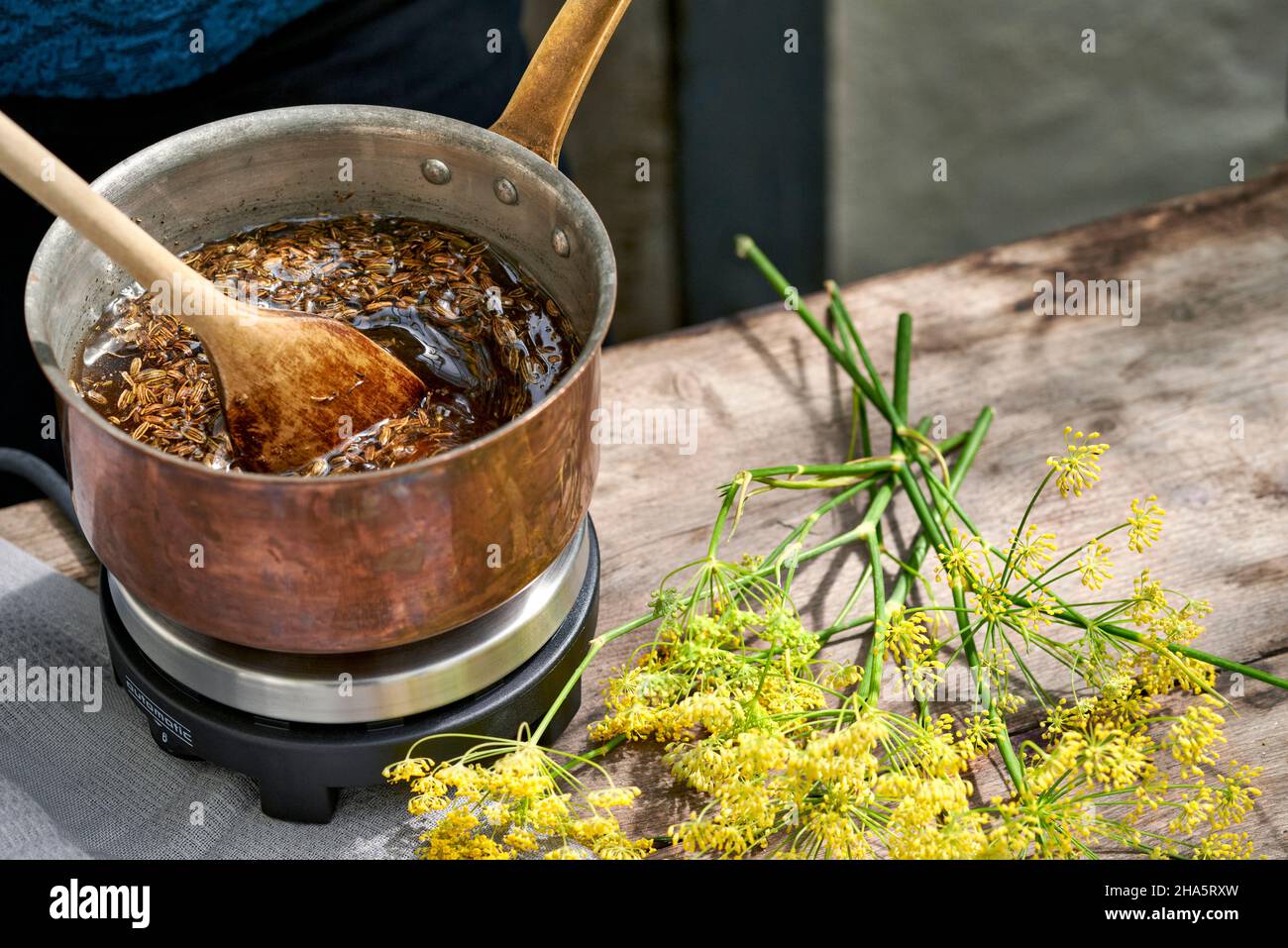 Arbeitsschritte mit Fenchelsamen und Fenchelsamen zur Herstellung von Fenchelsaft, mit einem Holzlöffel werden die Fenchelsamen zu einer Rohrzuckerlösung gerührt und erhitzt Stockfoto