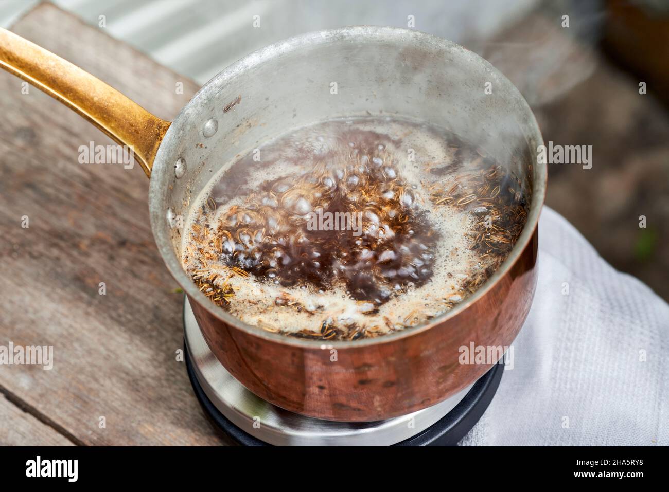 Arbeitsschritte mit Fenchel- und Fenchelsamen zur Herstellung von Fenchelsaft, Blick in einen Kupfertopf mit einer kochenden Lösung aus Fenchelsamen und Rohrzucker Stockfoto