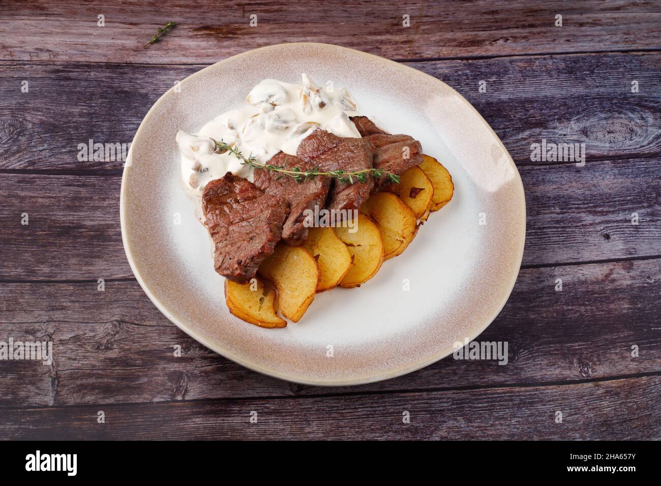 Dicke saftige Portionen gegrilltes Rinderfilet mit Pilzsauce Serviert mit Thymian-Kartoffeln auf einem alten Holztisch Stockfoto