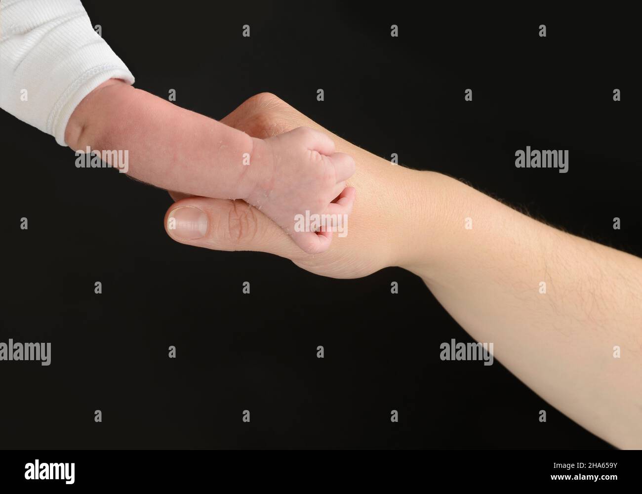 Nahaufnahme der Hand einer erwachsenen Person, die die Hand eines Babys berührt. Hände isoliert auf schwarzem Hintergrund. Stockfoto