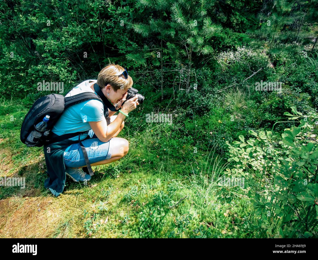 Eine Blondine mit kurzen Haaren macht ein Foto im hockenden Wald Stockfoto