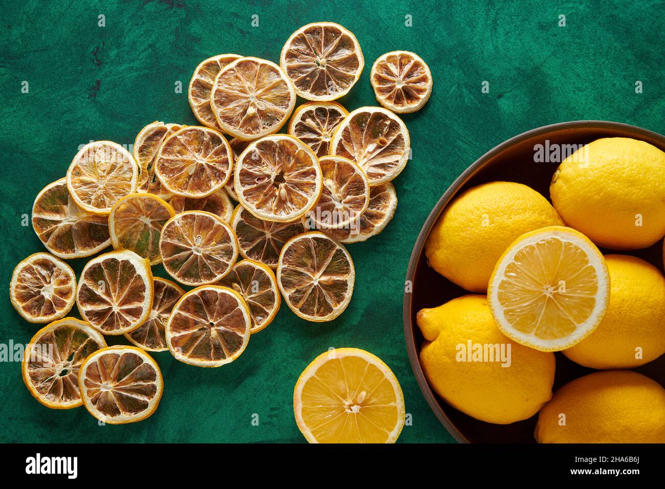 Getrocknete Zitronen auf grünem Hintergrund mit frischen Zitronen in einer Holzschale. Stockfoto