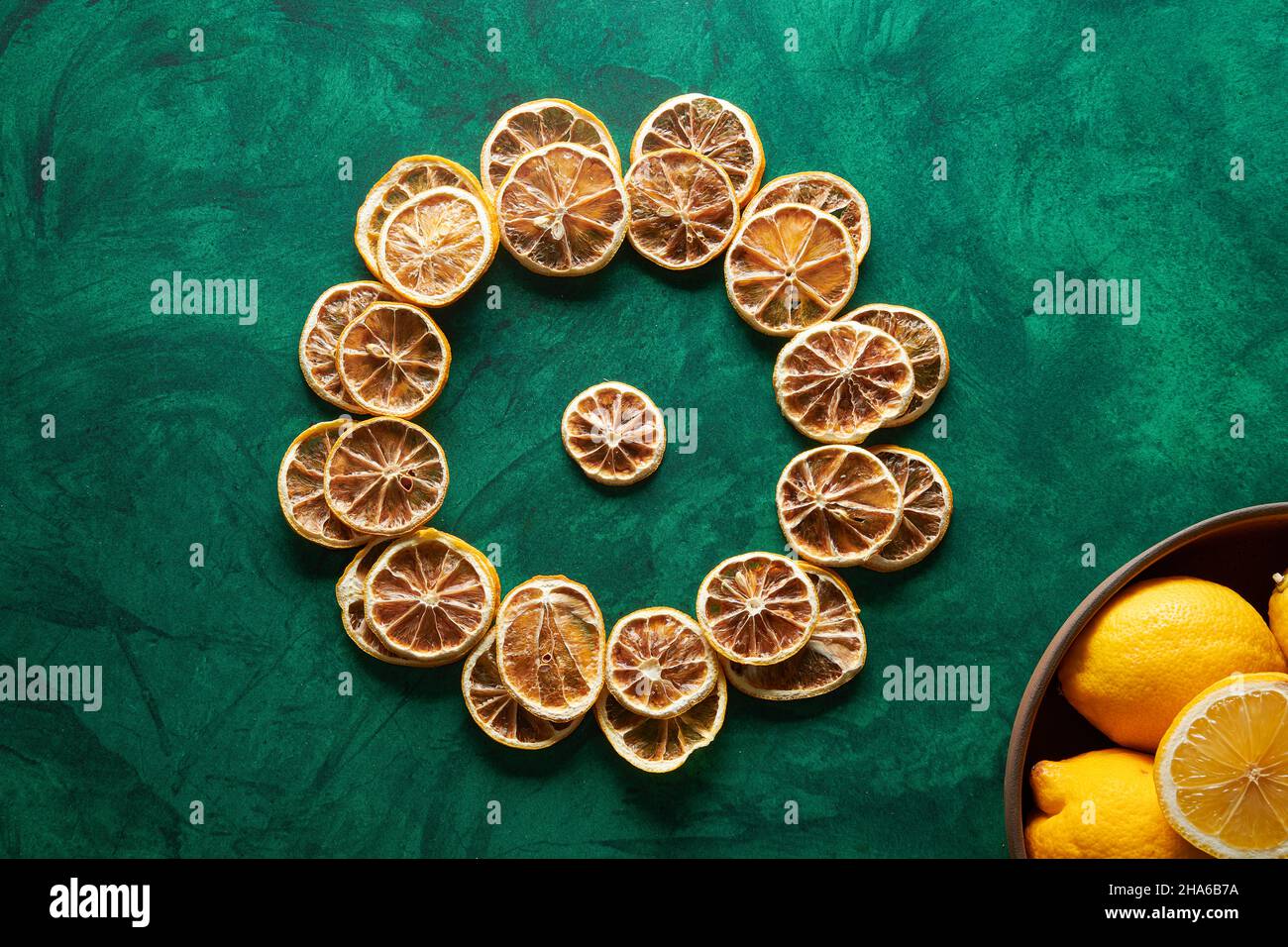 Getrocknete Zitronen auf grünem Hintergrund mit frischen Zitronen in einer Holzschale. Stockfoto