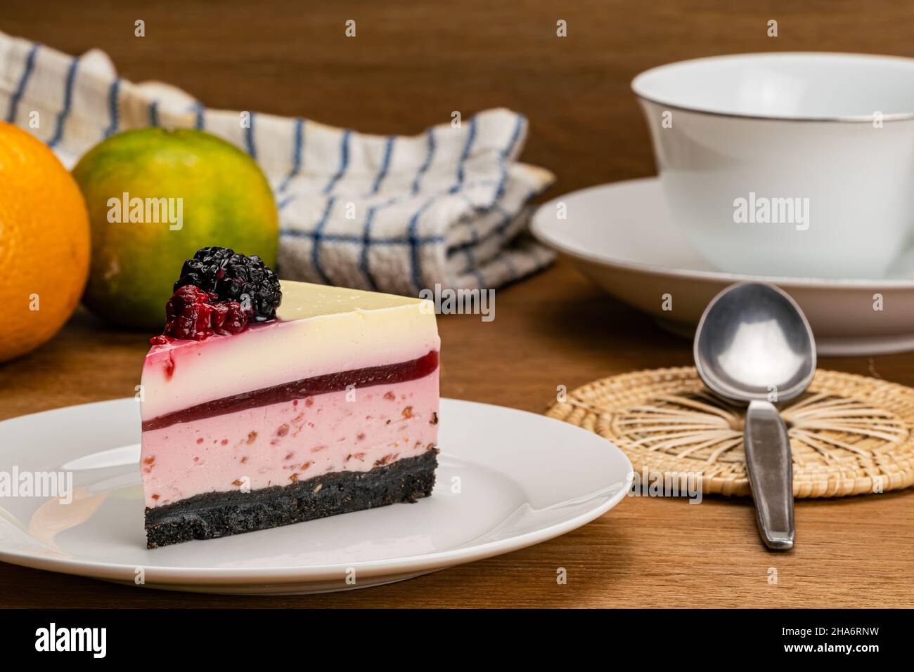 Seitenansicht des köstlichen Dessertstückes hausgemachter Himbeer-Käsekuchen, garniert mit konservierter Himbeere und Creme in weißer Keramikplatte, einer Tasse CO Stockfoto