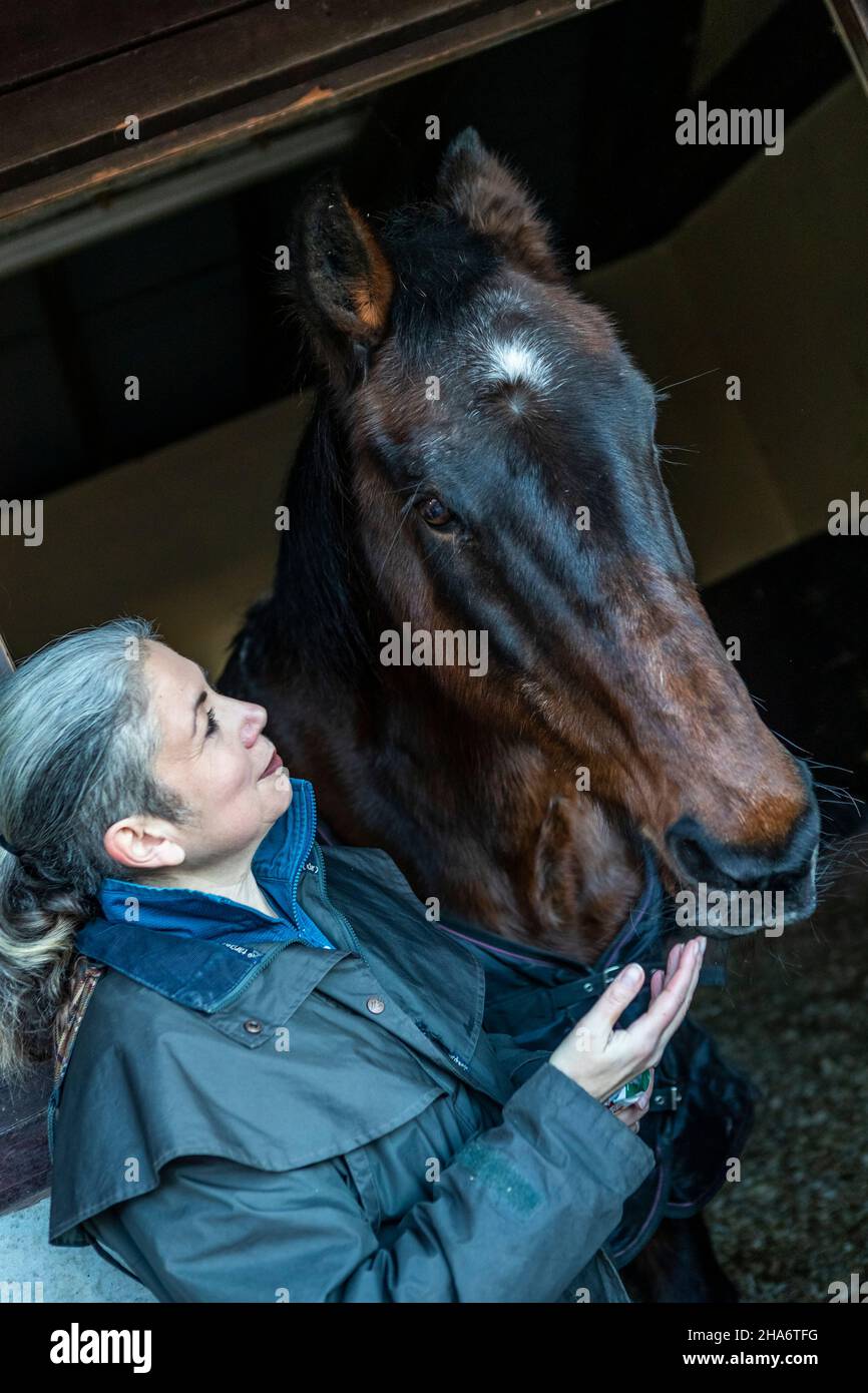 Eine reife Reiterin verbringt die letzten kostbaren Stunden, bevor ein Pferd aufgrund von schlechtem Gesundheitszustand und Alter abgesetzt wird. Stockfoto