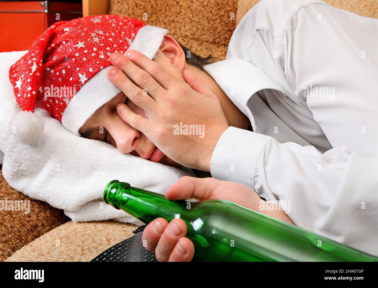 Betrunkener Teenager, der in Weihnachtsmütze schläft, und eine Flasche Bier  auf dem Sofa Stockfotografie - Alamy