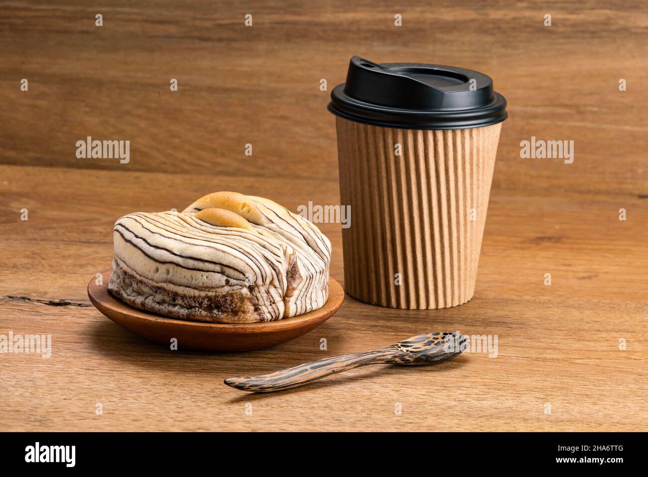 Blick auf das köstliche Frühstück Schokolade Flavored Brot auf Holzplatte mit Papiertasse Kaffee und Holzlöffel auf einem Tisch. Stockfoto