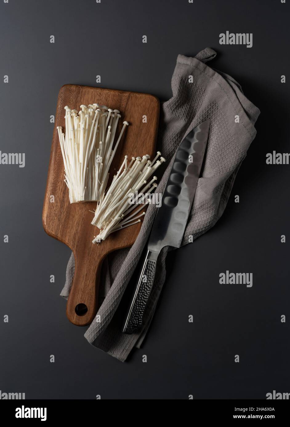 Enoki-Pilze, ein Messer und ein Schneidebrett auf schwarzem Hintergrund. Bild von Pilzen vor dem Kochen Stockfoto