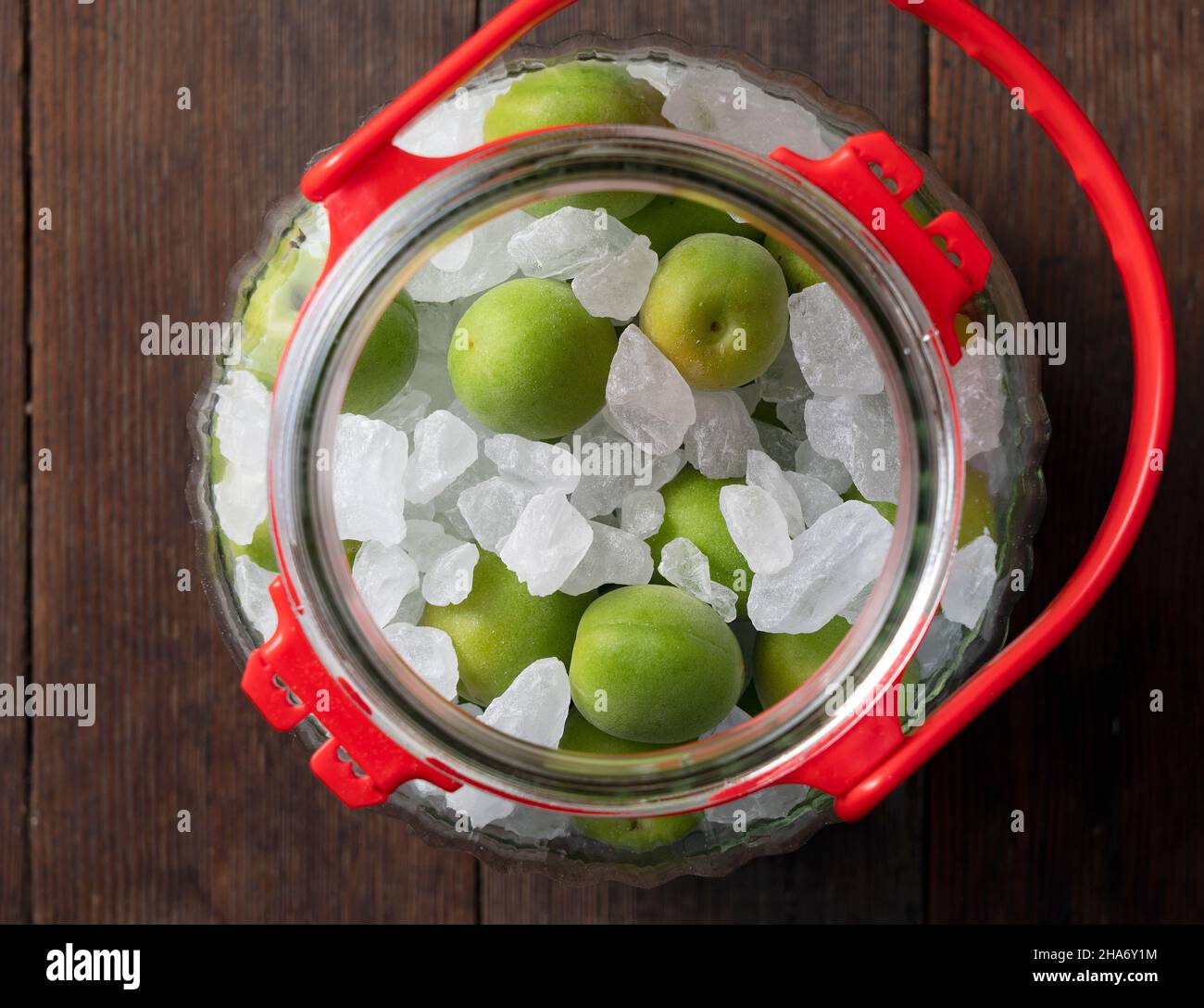 Unreife Ume-Frucht und Steinzucker auf einem hölzernen Hintergrund.Herstellung traditioneller japanischer grüner Pflaumenwein Stockfoto