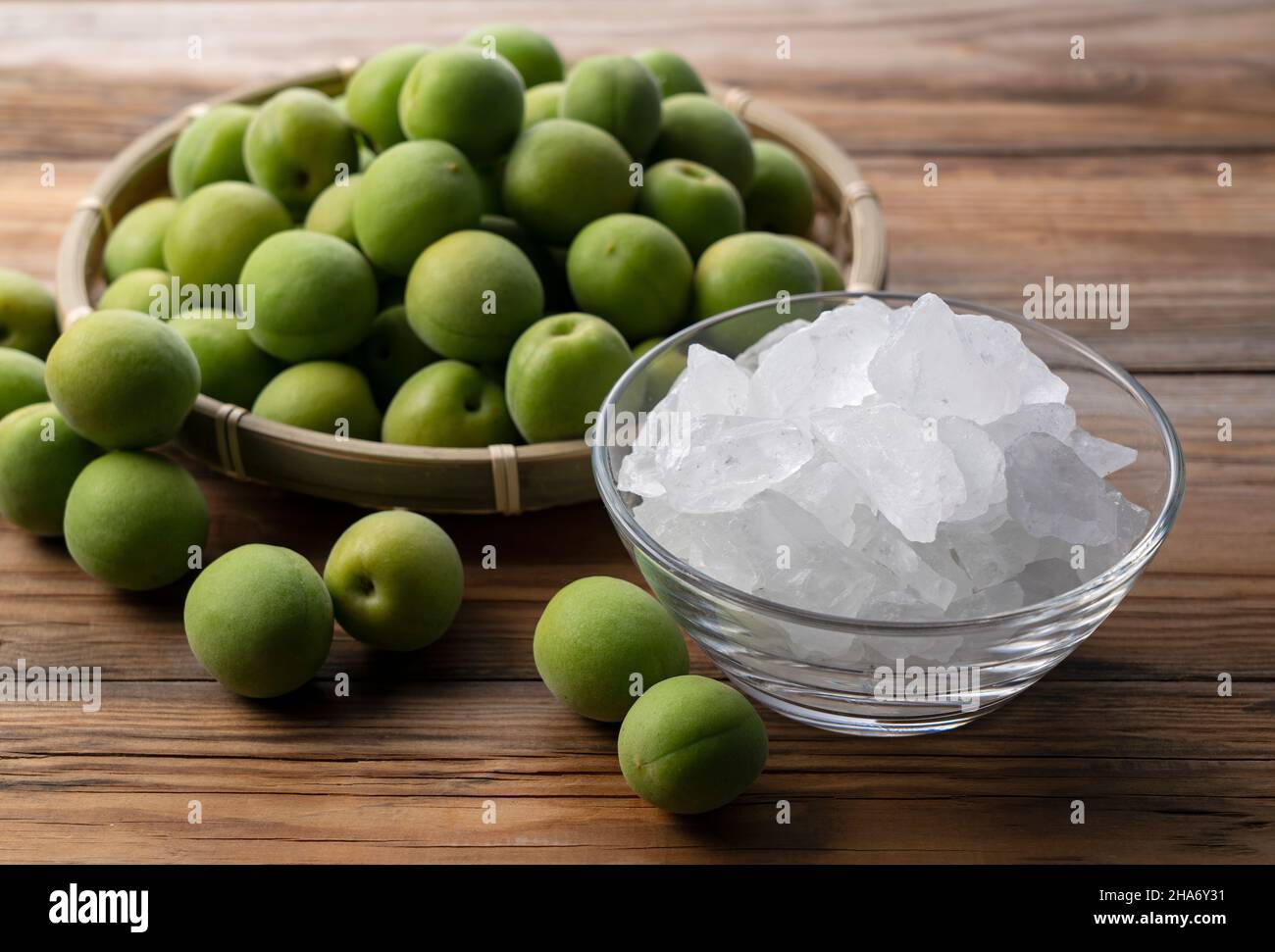 Unreife Ume-Frucht und Steinzucker auf einem hölzernen Hintergrund. Vorbereitung auf die Herstellung von japanischem Pflaumenwein Stockfoto