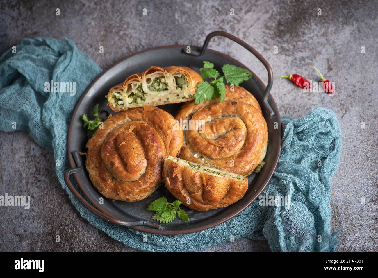 Hausgemachte vegane Mini-Pie mit Brennnesselpflanze in Form einer Schnecke auf rustikalem grauen Hintergrund. Vegane Küche. Stockfoto
