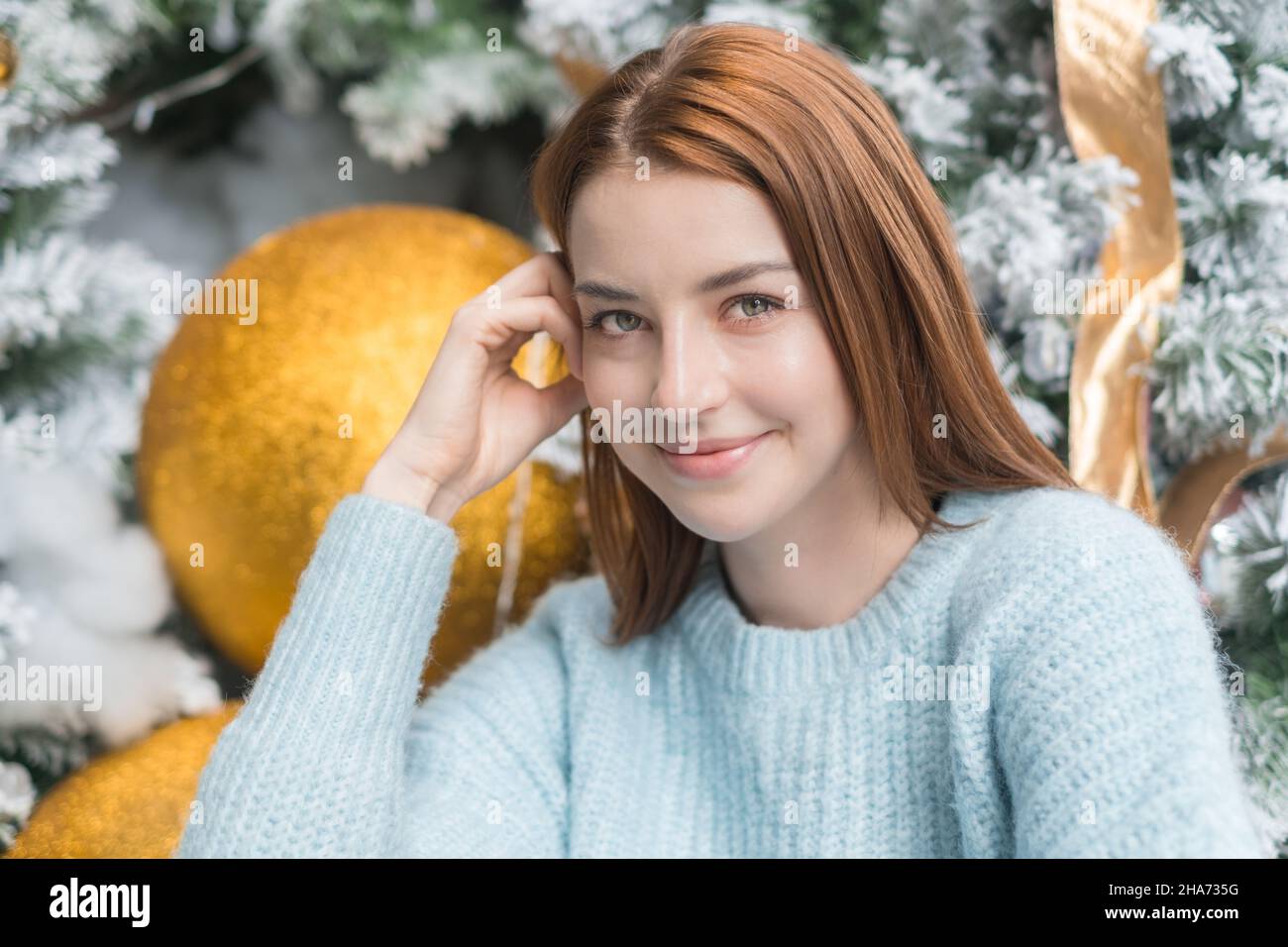 Neujahr Nahaufnahme Porträt von schönen lächelnden kaukasischen junge Frau in gemütlichen Wolle warm hellblau Pullover. Weihnachtsbaum im Hintergrund. Stockfoto