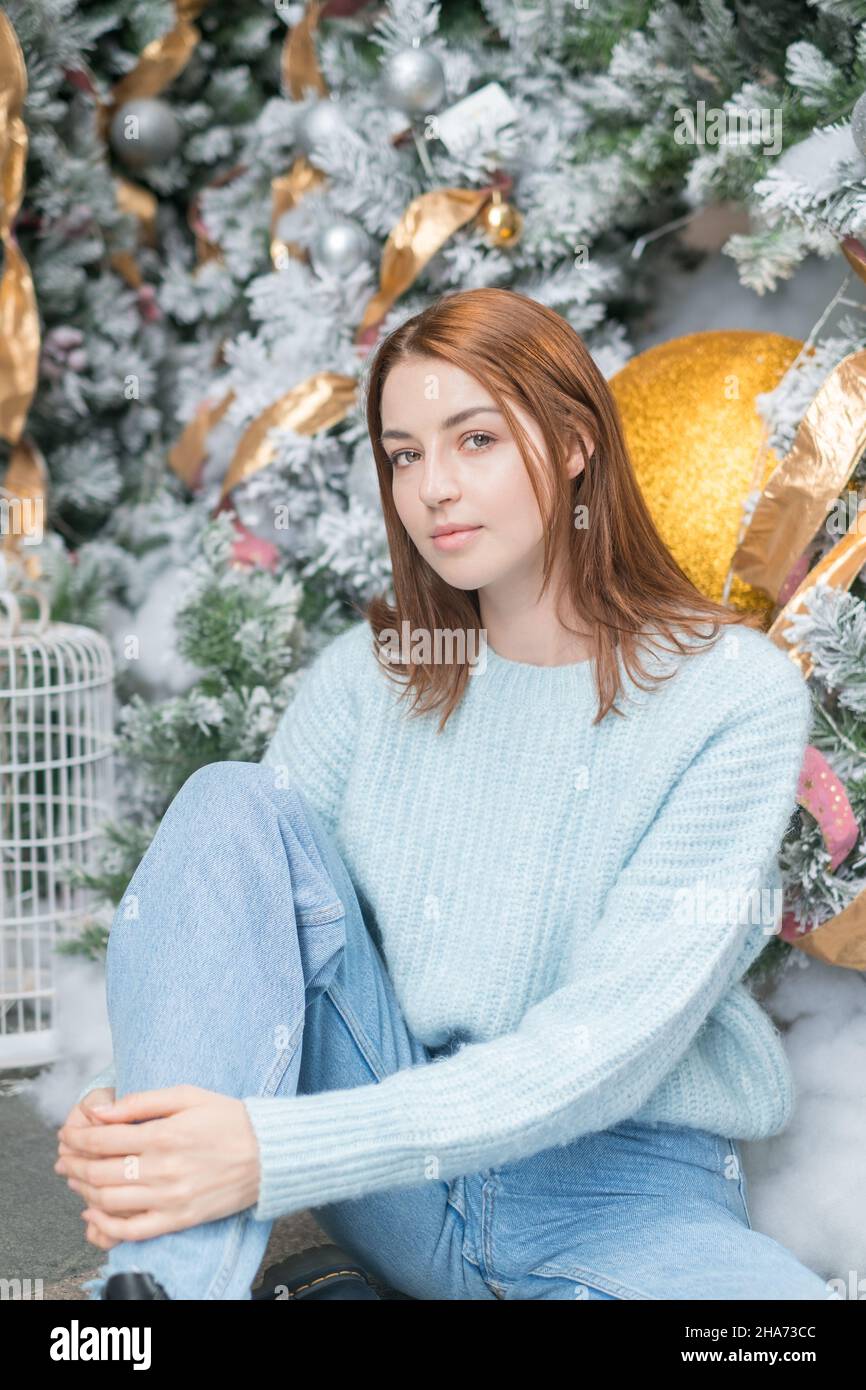 Neujahrs-Porträt der schönen kaukasischen jungen Frau in kuscheligen Wolle warm hellblau Pullover. Weihnachtsbaum auf dem Hintergrund.Weihnachts-Shooting Stockfoto