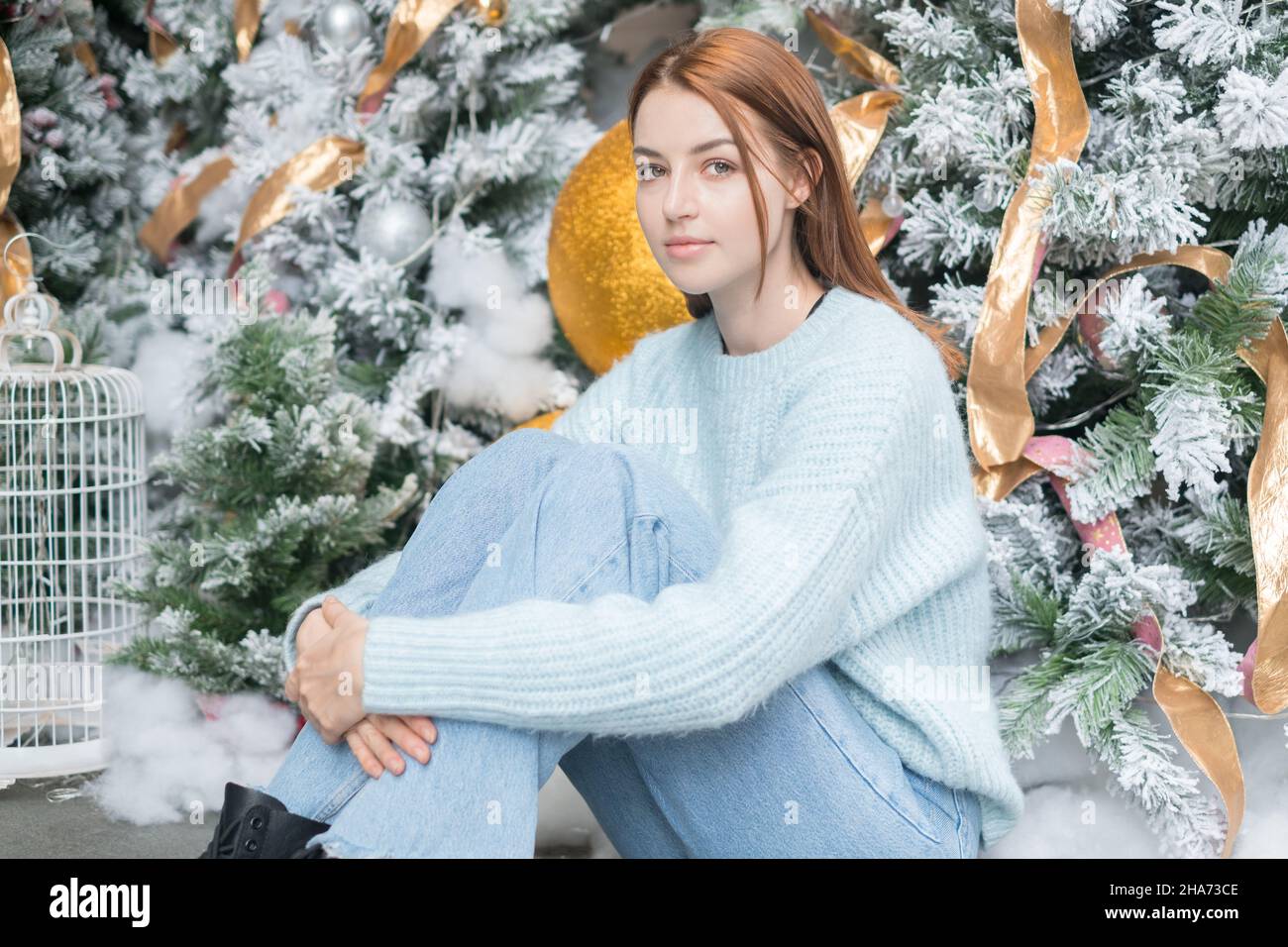Neujahrs-Porträt der schönen kaukasischen jungen Frau in kuscheligen Wolle warm hellblau Pullover. Weihnachtsbaum im Hintergrund. Weihnachts-Shooting Stockfoto