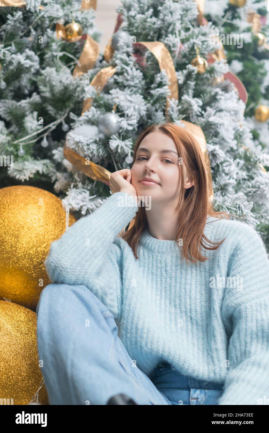 Neujahrs-Porträt der schönen kaukasischen jungen Frau in kuscheligen Wolle warm hellblau Pullover. Weihnachtsbaum im Hintergrund. Weihnachts-Shooting Stockfoto