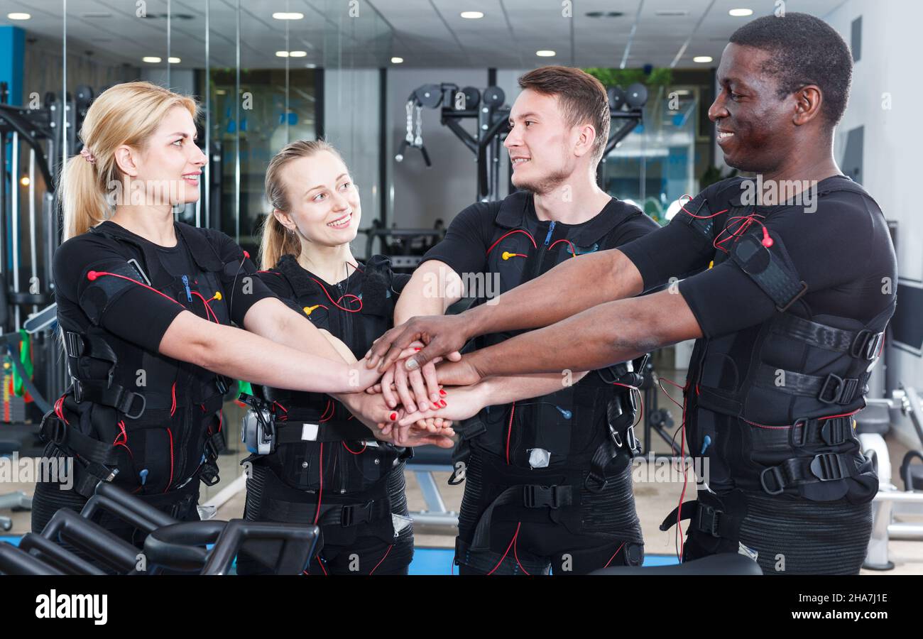 Lächelnde Menschen in Topform, die während des EMS-Trainings im Fitnessstudio Pause machen und zusammen posieren Stockfoto