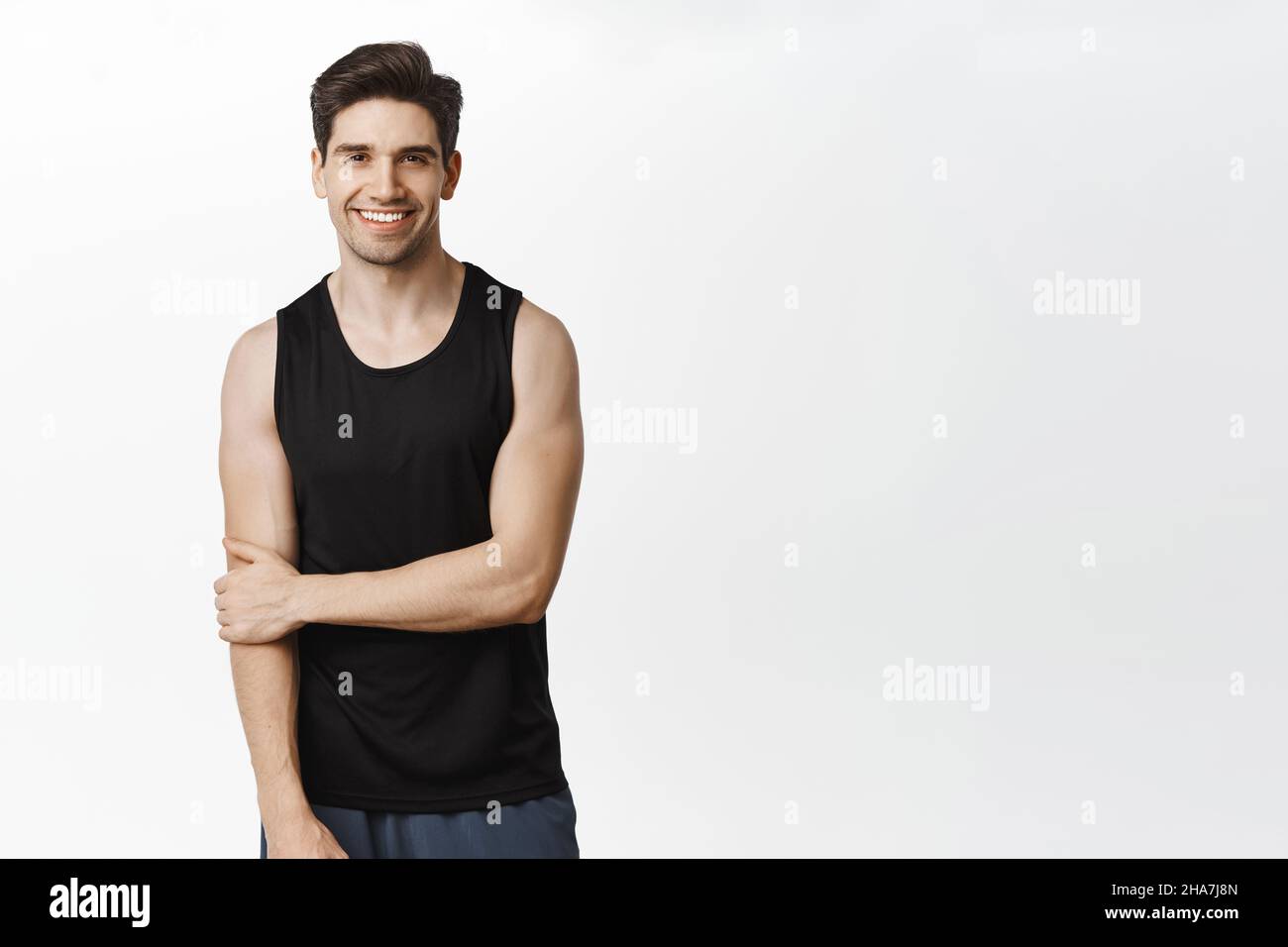 Sport und Workout. Schöner lächelnder Mann posiert in Tank Top vor weißem Studio-Hintergrund Stockfoto