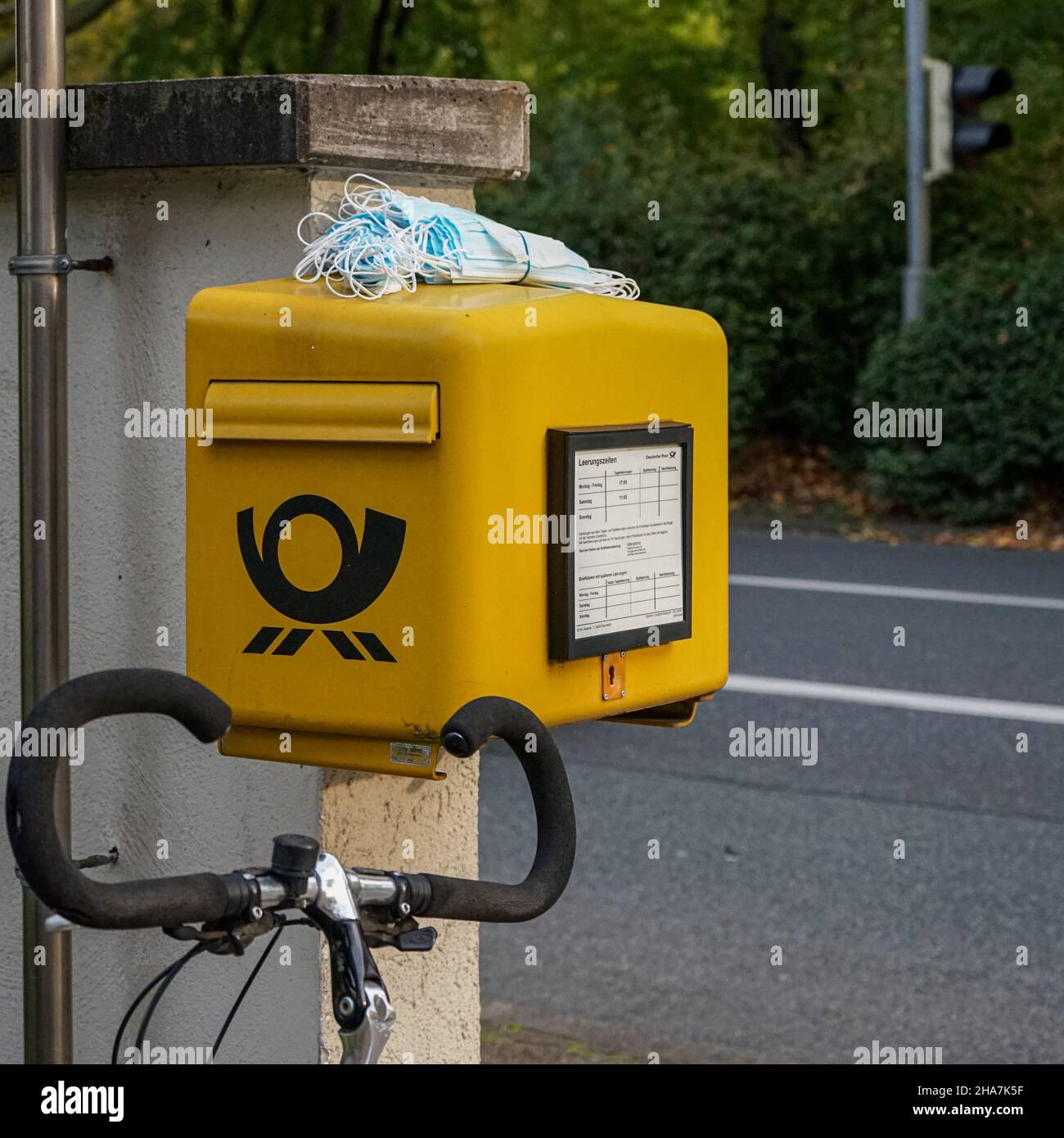Auf einen gelben Briefkasten der Deutschen Post hat jemand einen Haufen Corona-Masken gelegt. Davor steht ein Fahrrad, der Lenker ist zu sehen. Stockfoto