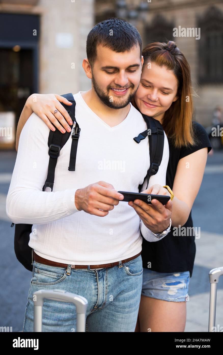 Fröhliche junge weibliche und männliche Touristen zusammen am Handy suchen Stockfoto