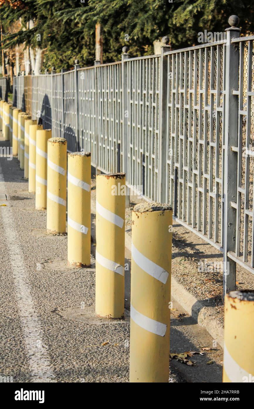 Gelbe Poller schützen einen Metallzaun. Poller auf der Straße. Stockfoto