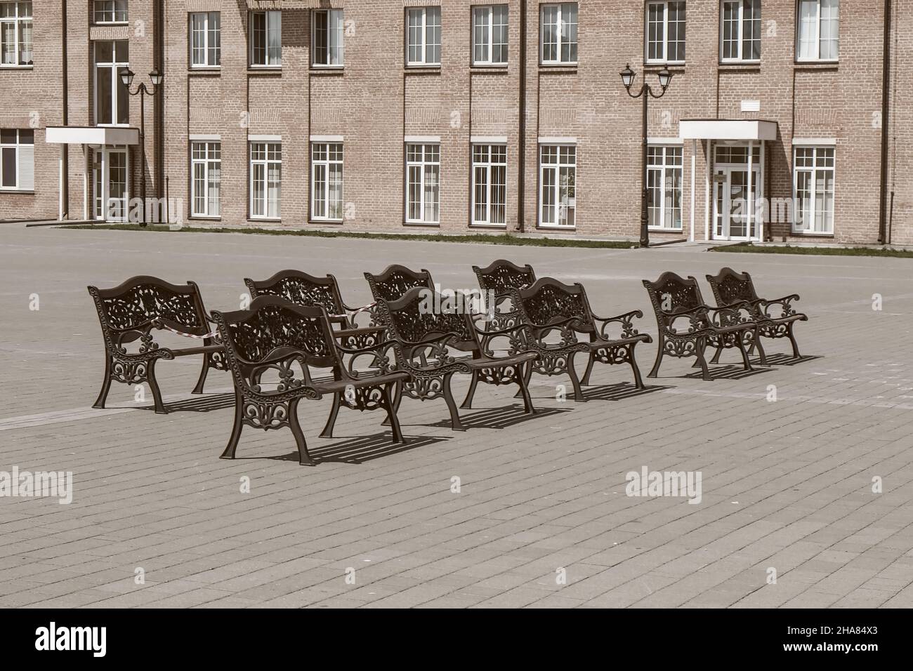 Reihe leerer Vintage-Holzbänke mit verziertem schwarzem Eisen, geschmiedeten Elementen in Sepia-Tönen. Städtische öffentliche vandalensichere Möbel. Öffentliche Stadt Ruhebereich Stockfoto