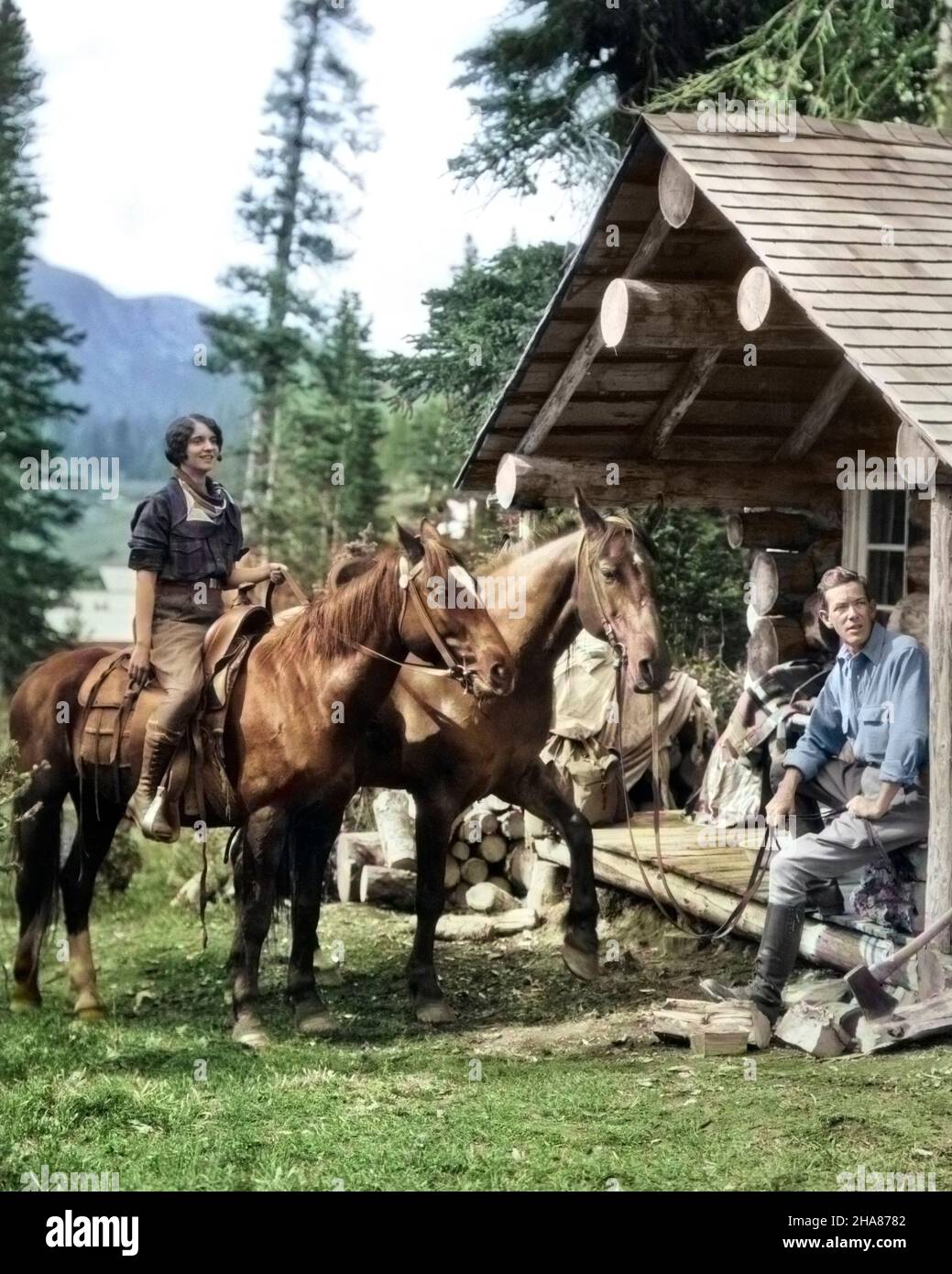 1920S PAAR VOR DER BLOCKHÜTTE FRAU AUF PFERD MANN SITZT AUF DER VERANDA UND HÄLT DIE ZÜGEL DES ZWEITEN PFERDES ASSINIBOINE KANADA - C3530C HAR001 HARS URLAUB KIEFER LIFESTYLE ARCHITEKTUR FRAUEN VERHEIRATET LÄNDLICHEN EHEGATTEN EHEMÄNNER ERWACHSENE KOPIEREN RAUM IN VOLLER LÄNGE HALBLANGE DAMEN PERSONEN SATTEL ERWACHSENE MÄNNER GEBÄUDE HÜTTE RAU NORDAMERIKA NORDAMERIKA ERHOLUNG CAMPING ZEIT WEG PFERD ZÜGEL SÄUGETIERE ABENTEUER LOG KURZURLAUB KANADISCHE ERHOLUNG RICHTUNG URLAUB ASSINIBOINE WILDNIS STRUKTUREN ZWEITE STILVOLLE ARCHITEKTUR DETAIL ARCHITEKTUR GROBE SÄUGETIER MITTLEREN ERWACHSENEN MANN MITTLEREN ERWACHSENEN FRAU Stockfoto