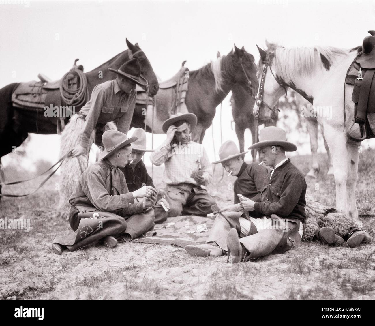 1920S COWBOYS UND IHRE PFERDE SITZEN AUF DEM BODEN UND SPIELEN POKER UM EINE INDISCHE DECKE, DIE HÜTE TRÄGT UND ZIGARETTEN RAUCHT - H879 HAR001 HARS MALES WESTERN TRANSPORTATION MIDDLE-AGED S/W RUHT MAN-AGED MAN CIGARETTES COWBOYS FREIHEIT GLÜCKSSPIEL GLÜCK POKER SÄUGETIERE ABENTEUER FREIZEIT PALS LOW-ANGLE-BERUFE KARTENSPIEL FREUNDLICH GAMBLE WAGER CHAPS SÄUGETIER MITTLEREN ERWACHSENEN MITTLEREN ERWACHSENEN MANN ZWEISAMKEIT JUNGEN ERWACHSENEN MANN WETTE WETTEN SCHWARZ UND WEISS CHANCE HAR001 ALTMODISCH Stockfoto